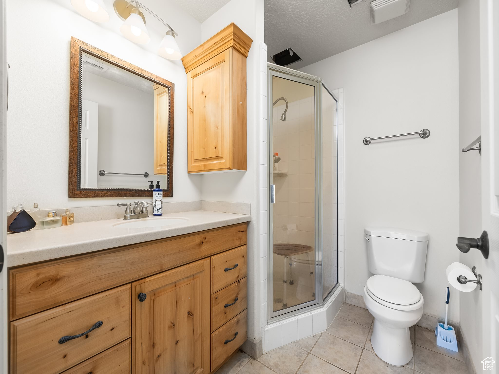 Bathroom featuring tile patterned floors, toilet, a shower with door, and vanity
