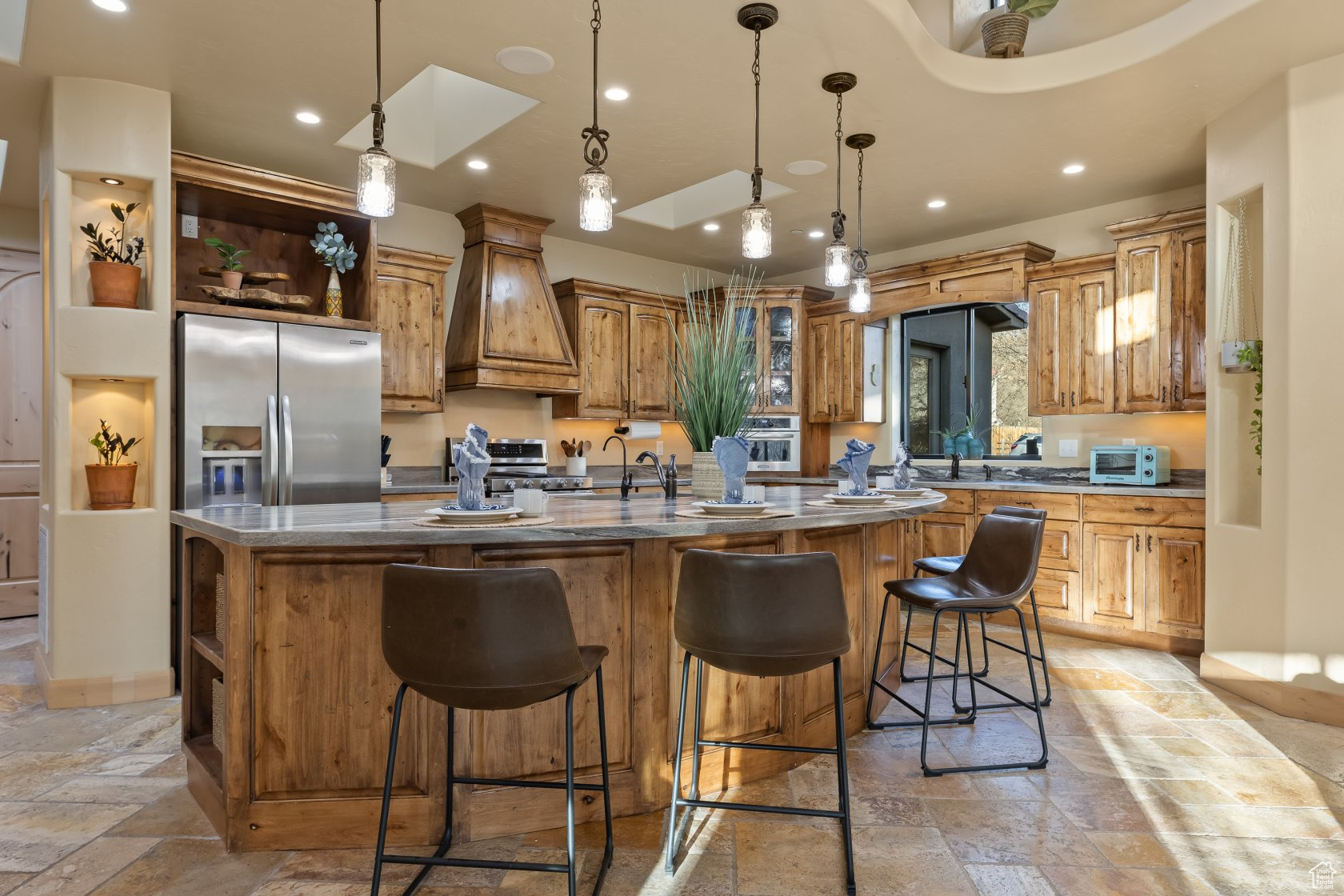 Kitchen featuring premium range hood, hanging light fixtures, stainless steel appliances, a kitchen bar, and a large island with sink