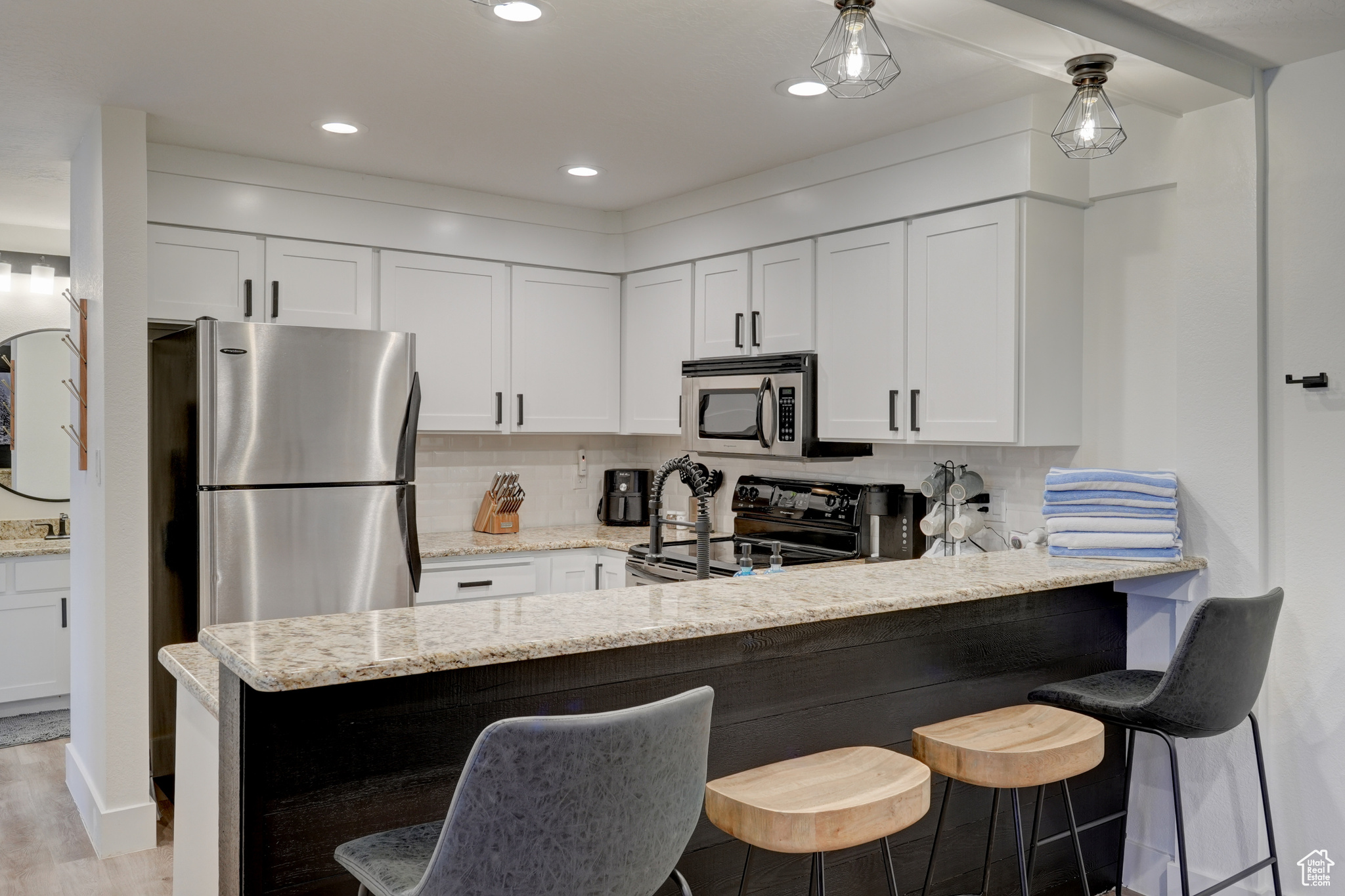 Kitchen with stainless steel appliances, white cabinetry, and light stone counters