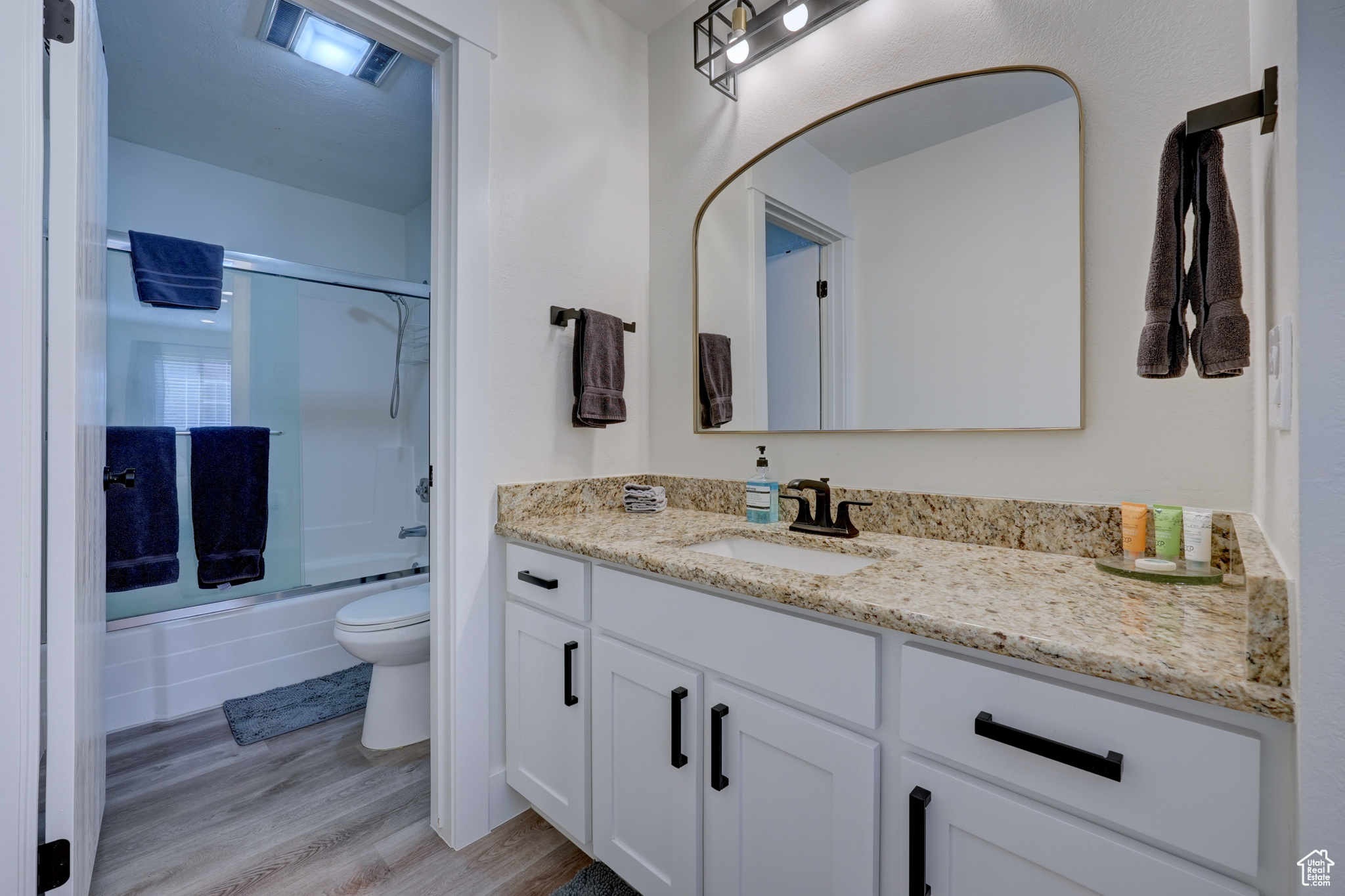 Full bathroom with toilet, wood-type flooring, shower / bath combination with glass door, and vanity