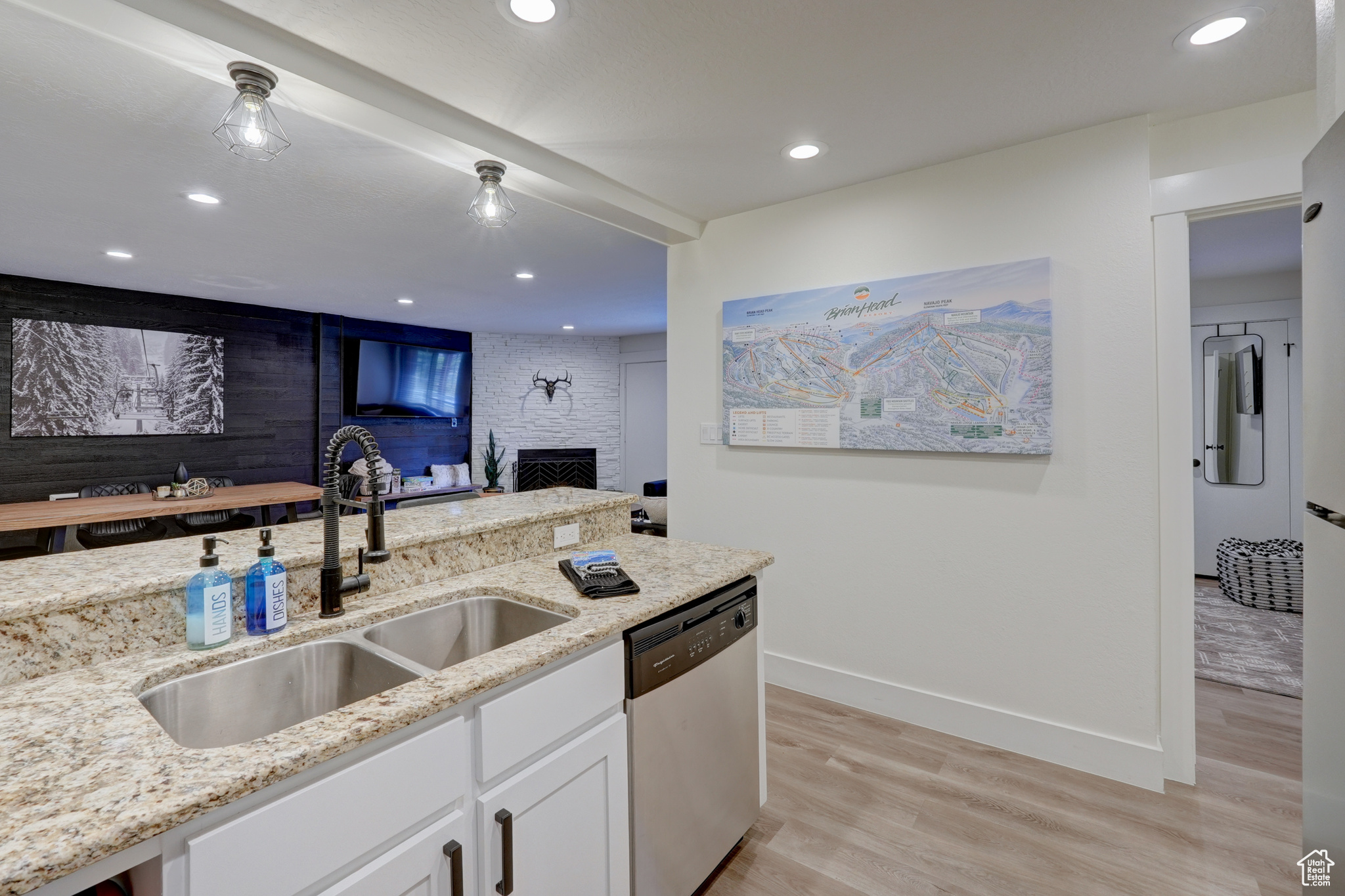 Kitchen with stainless steel dishwasher, light stone countertops, sink, and white cabinets