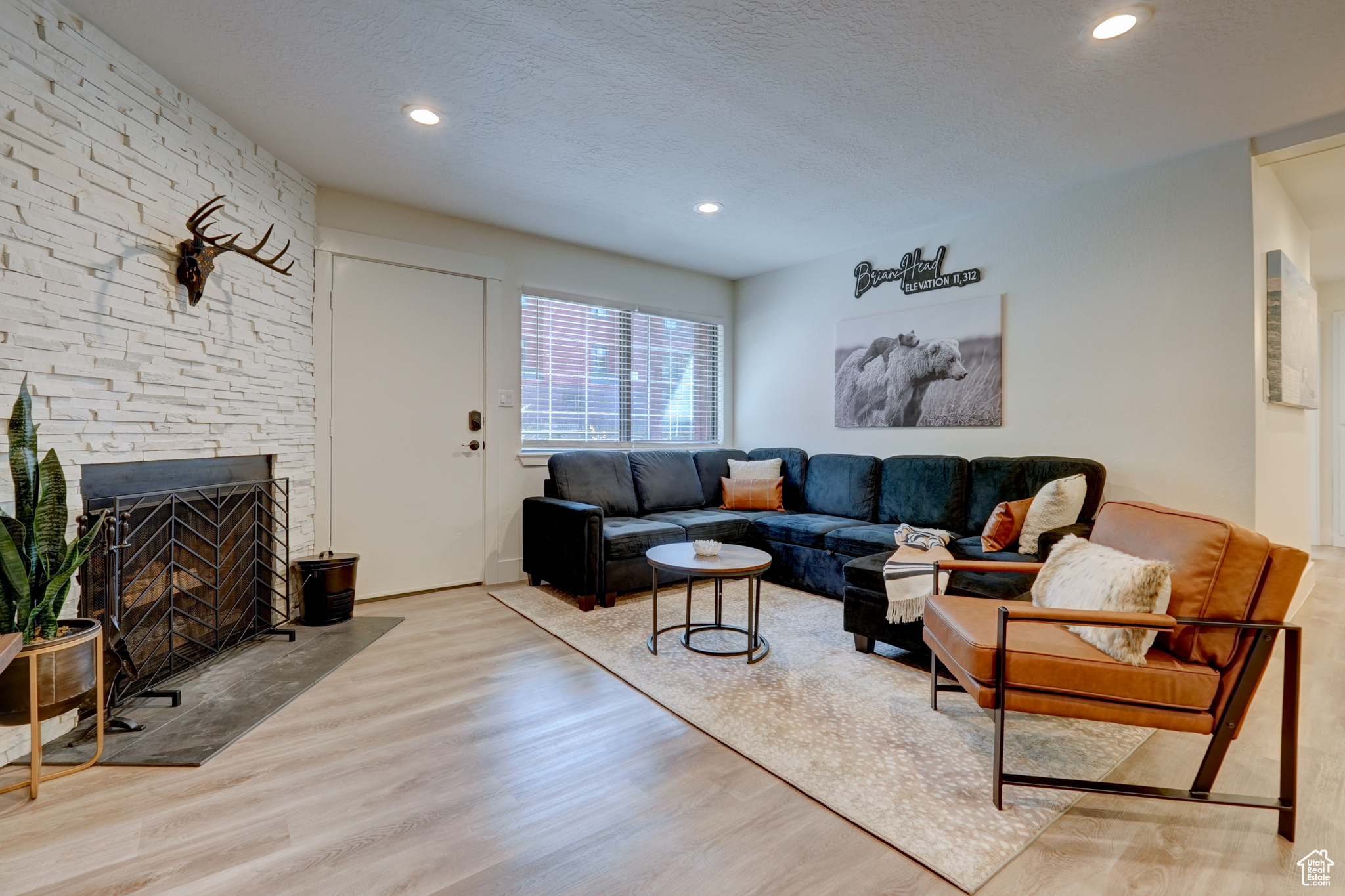 Living room featuring a stone fireplace, a textured ceiling, and light wood-type flooring