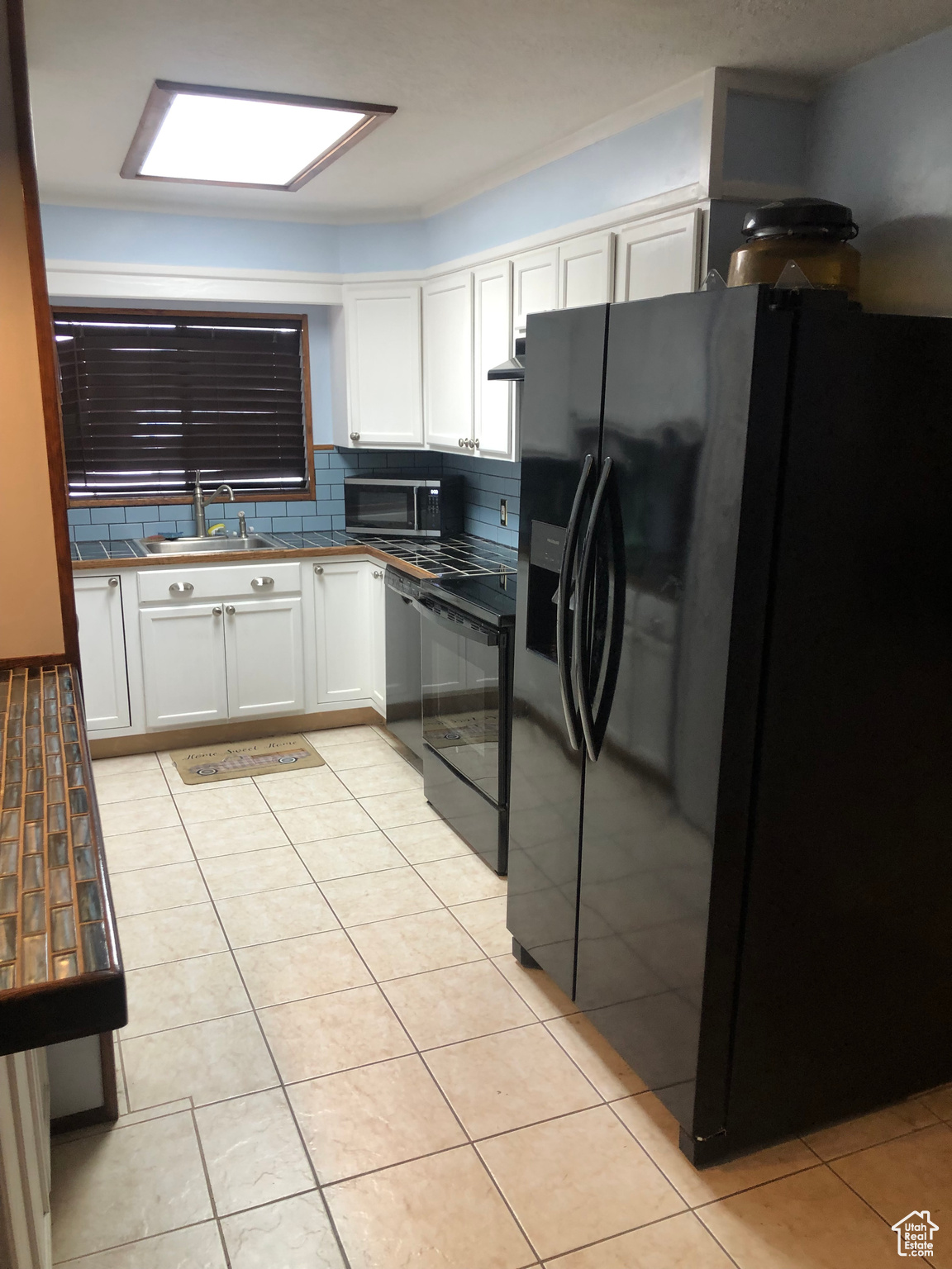 Kitchen with sink, tasteful backsplash, black appliances, light tile patterned floors, and white cabinets