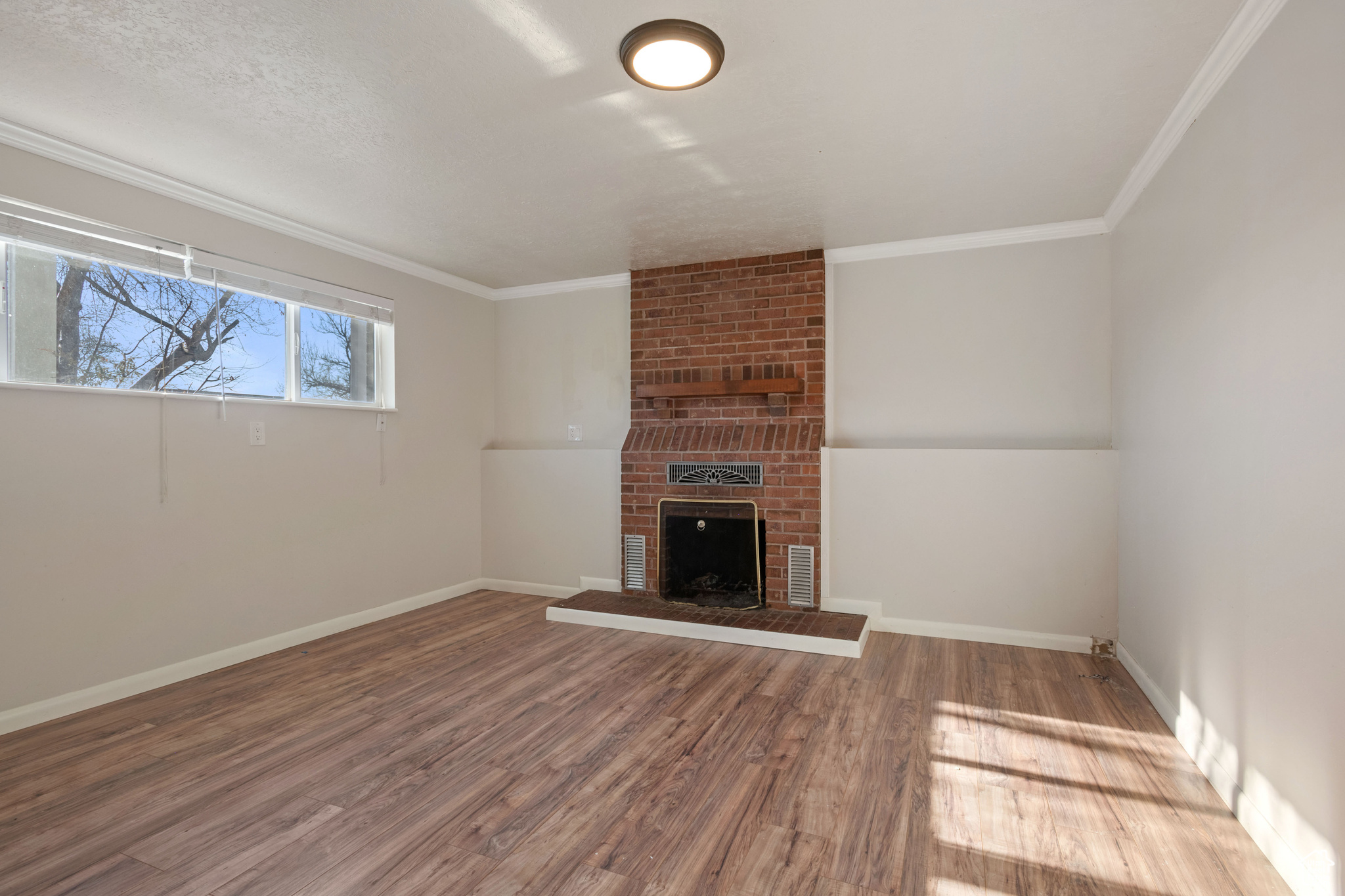 Unfurnished living room featuring crown molding, a brick fireplace, and hardwood / wood-style floors