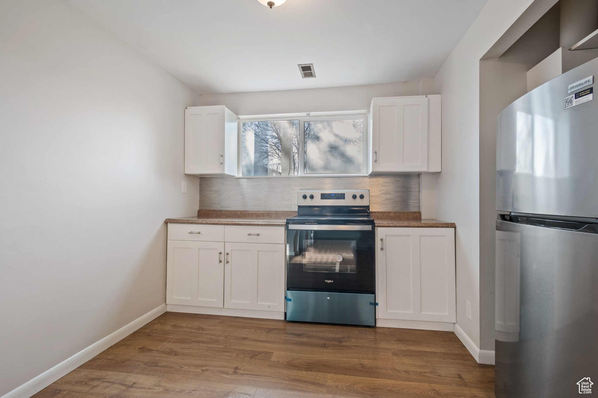 Kitchen featuring stainless steel appliances, white cabinetry, hardwood / wood-style flooring, and decorative backsplash