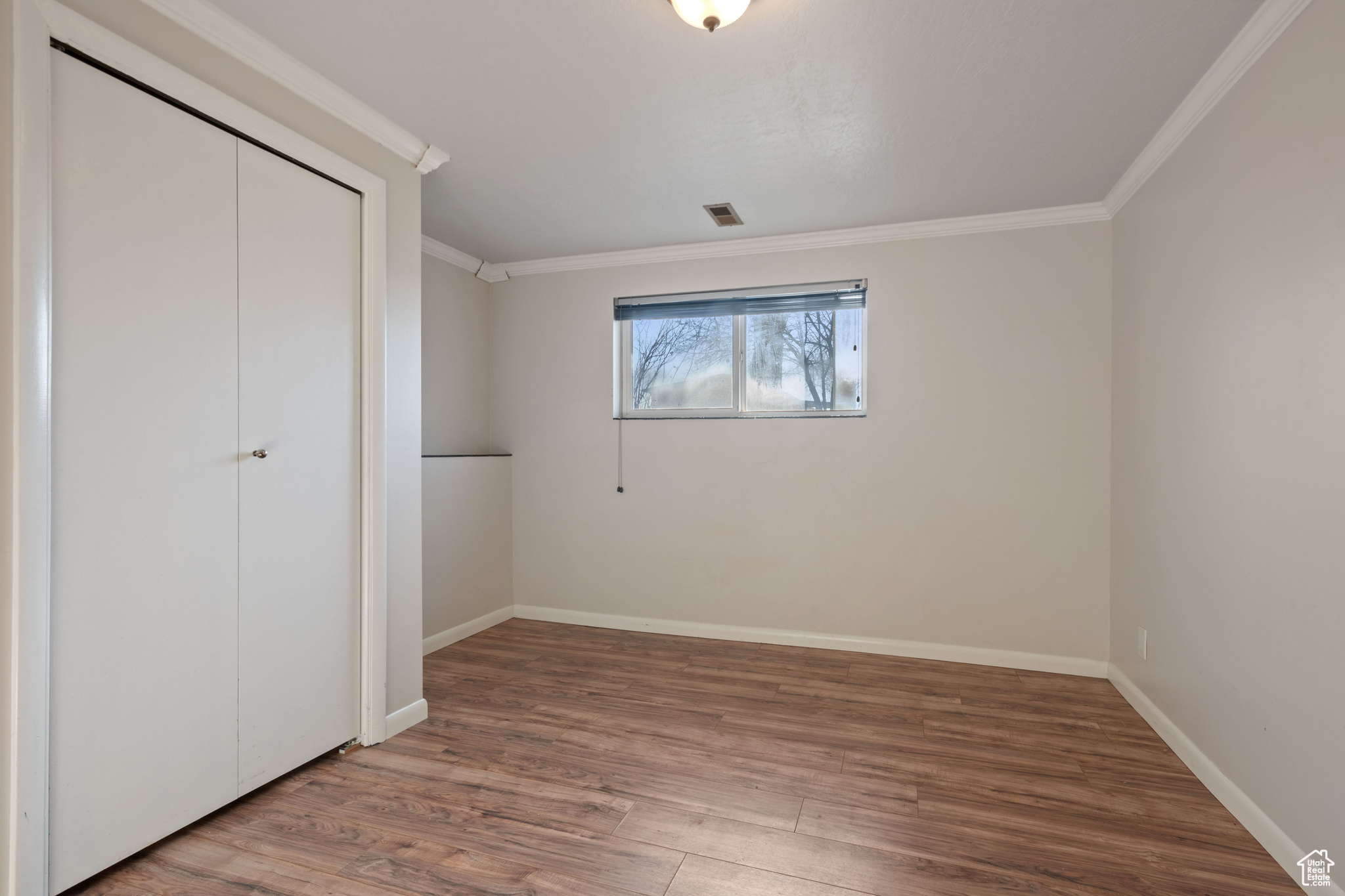 Unfurnished bedroom with ornamental molding, wood-type flooring, and a closet