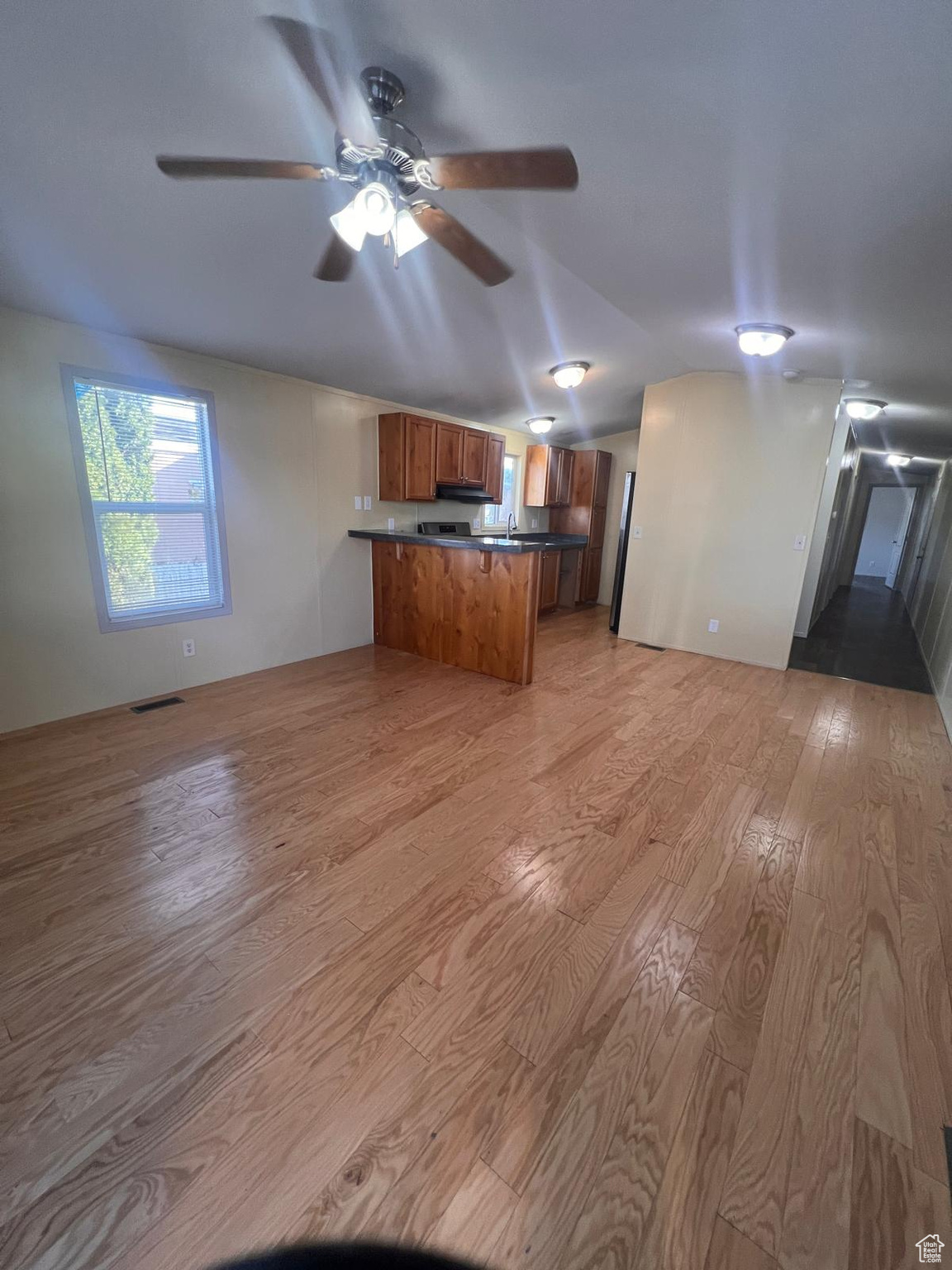 Kitchen featuring brown cabinetry, light wood-type flooring, a peninsula, dark countertops, and open floor plan