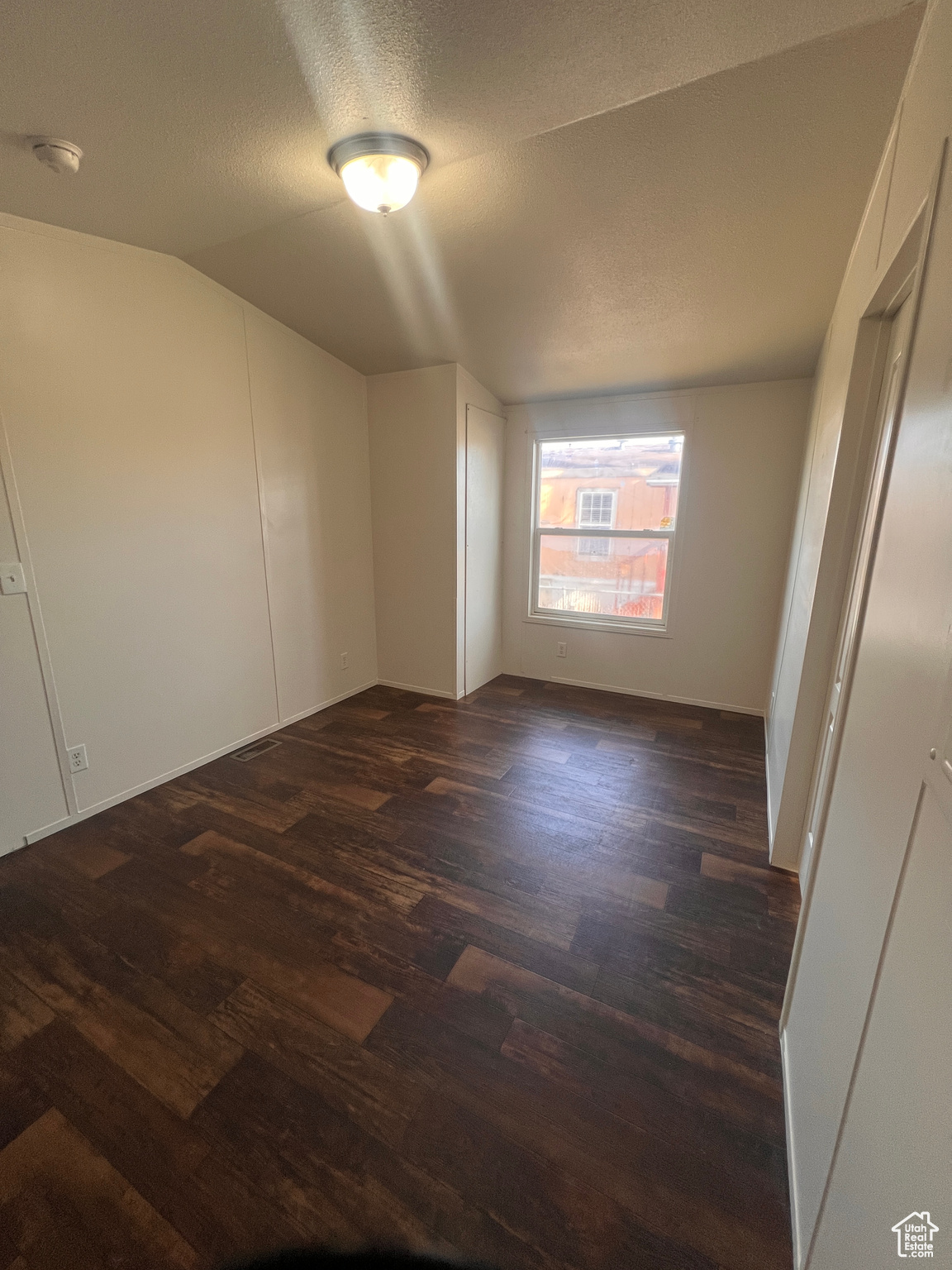 Unfurnished room featuring a textured ceiling, dark wood-type flooring, and vaulted ceiling