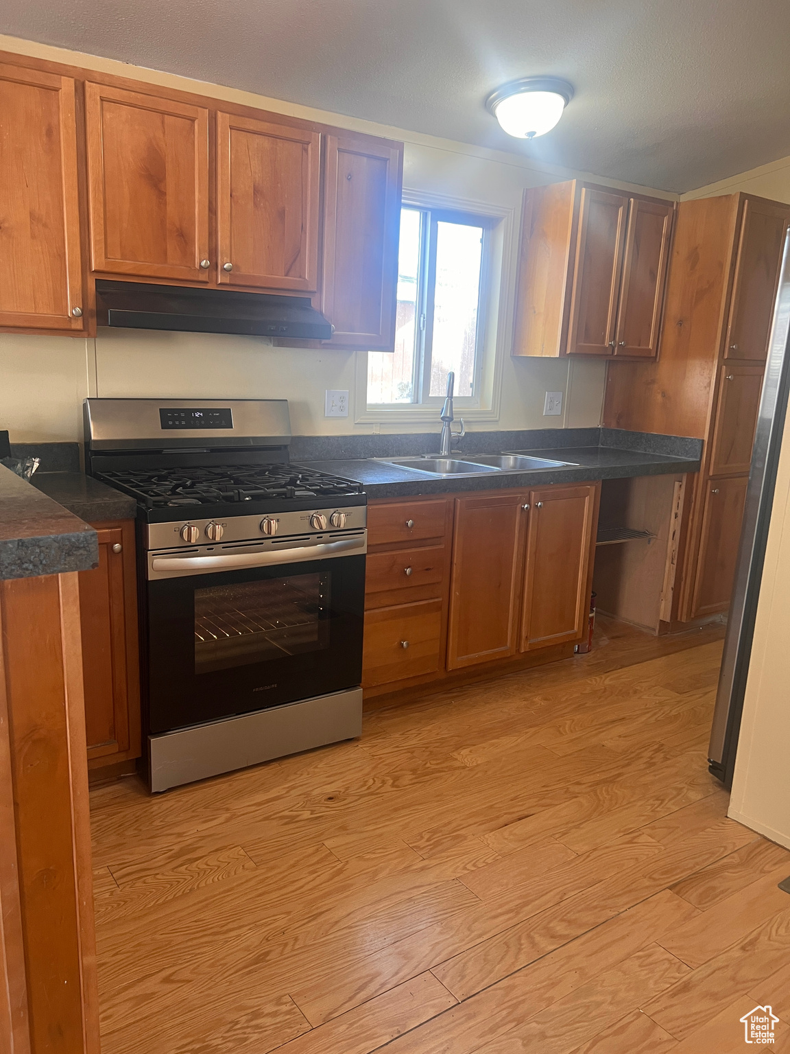 Kitchen with under cabinet range hood, a sink, dark countertops, light wood-style floors, and gas range