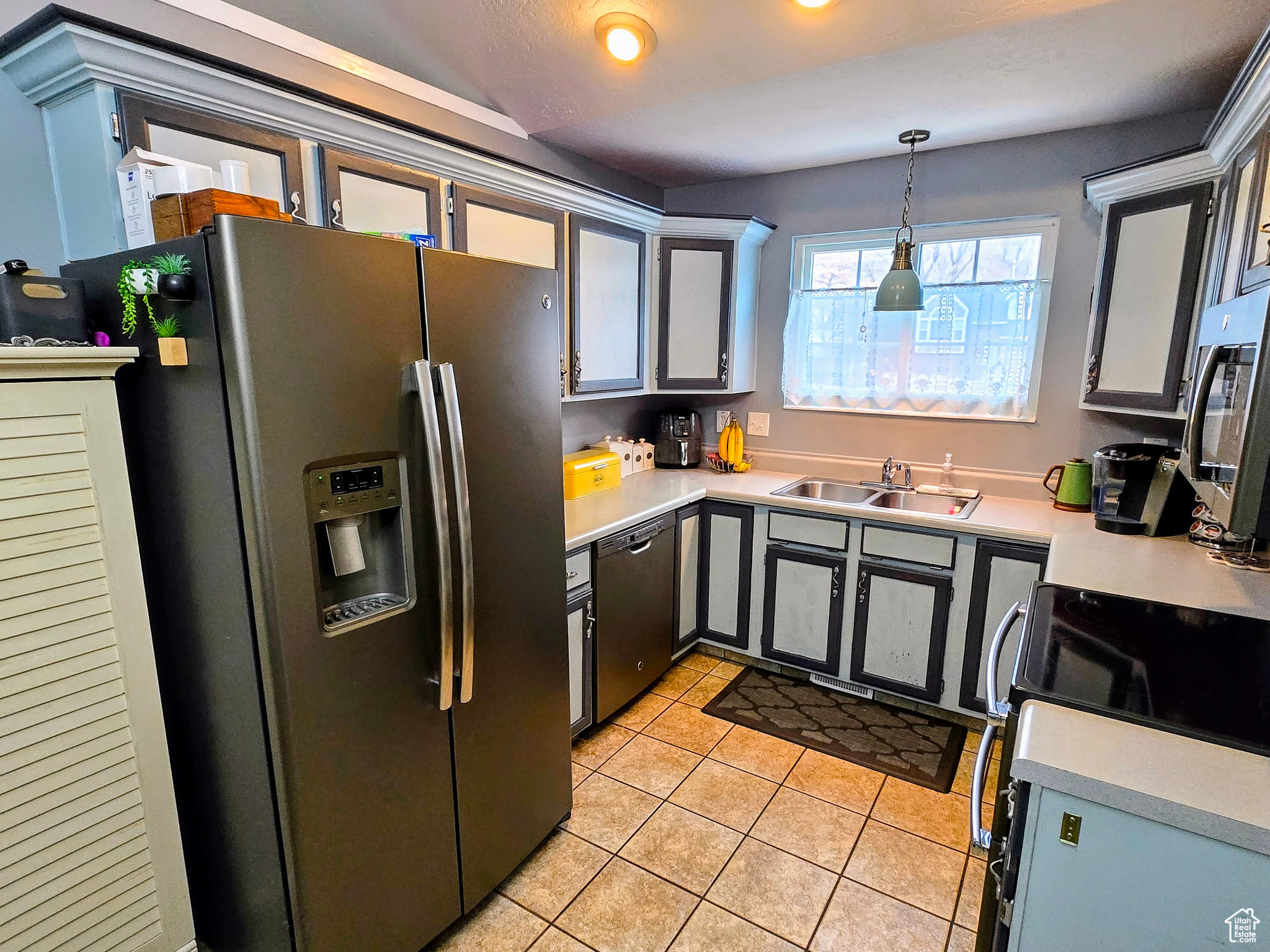 Kitchen featuring sink, light tile patterned floors, gray cabinets, appliances with stainless steel finishes, and hanging light fixtures