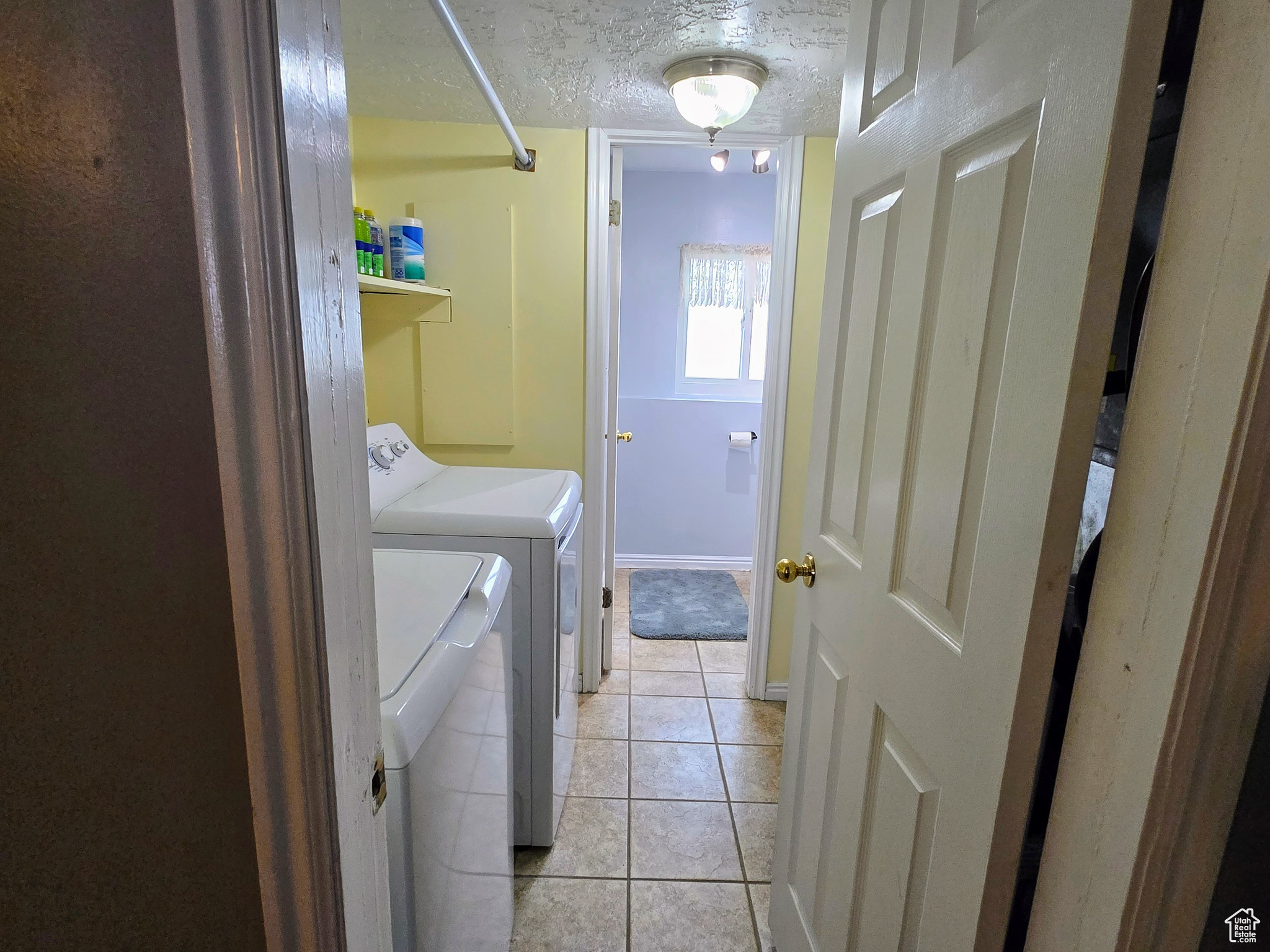 Washroom with light tile patterned flooring, washer and dryer, and a textured ceiling