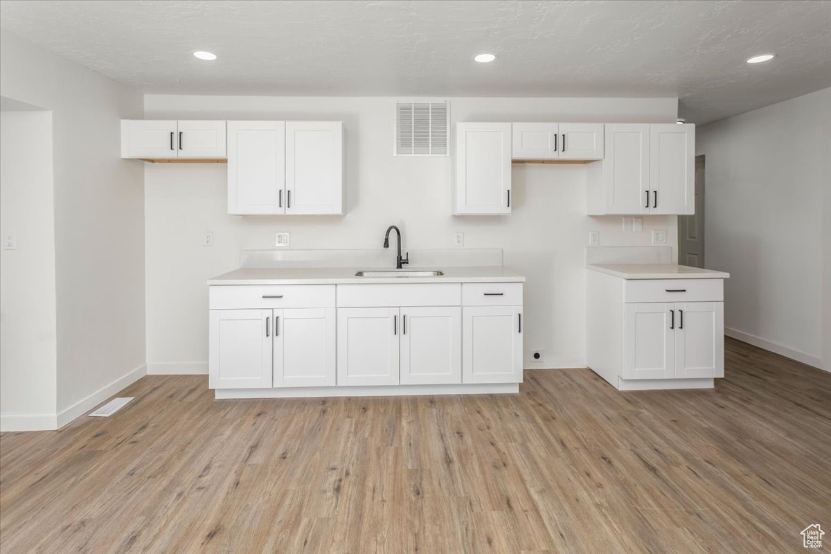 Kitchen featuring white cabinetry, sink, light hardwood / wood-style floors, and a textured ceiling