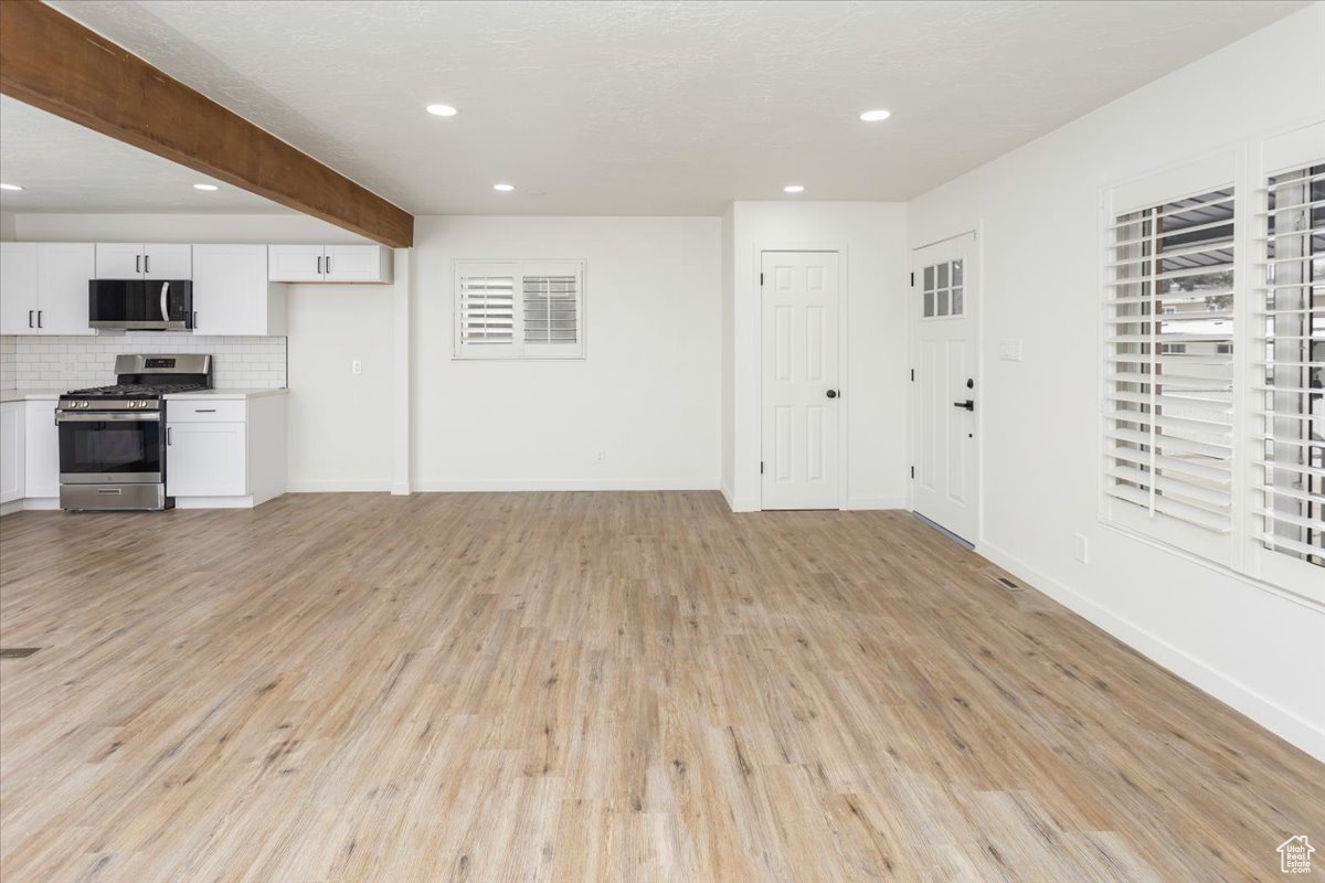 Unfurnished living room with beam ceiling and light hardwood / wood-style flooring