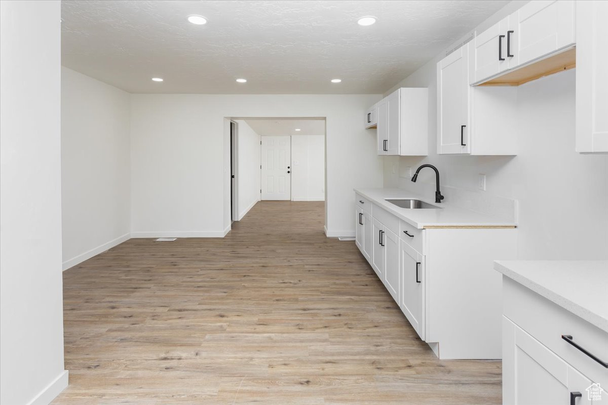 Kitchen featuring light hardwood / wood-style floors, sink, a textured ceiling, and white cabinets