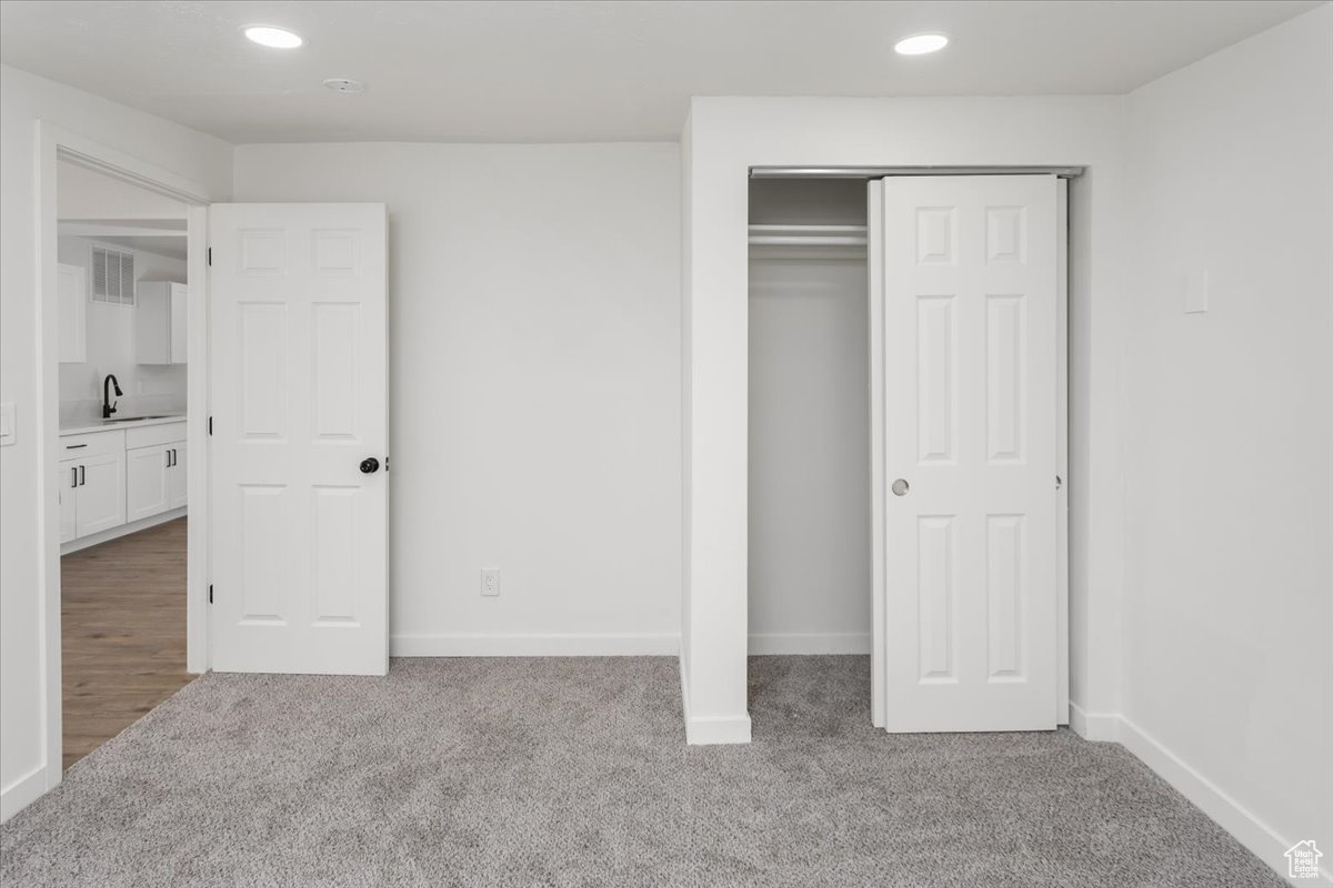 Unfurnished bedroom with a closet, sink, and light carpet