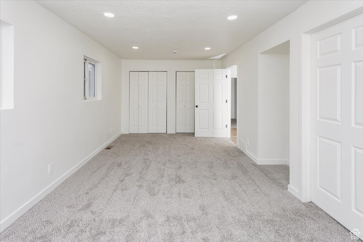 Unfurnished bedroom with multiple closets, light carpet, and a textured ceiling
