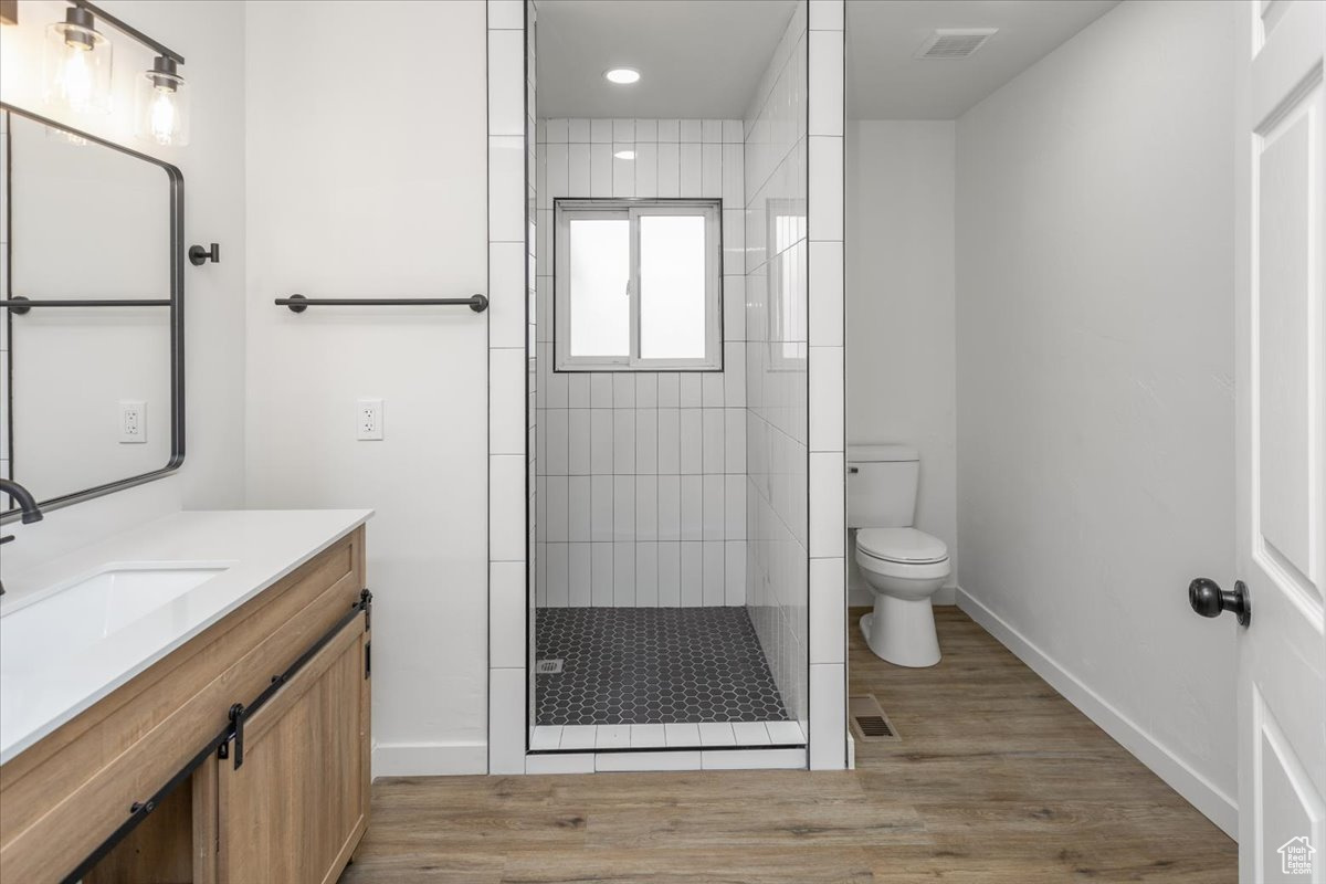 Bathroom featuring vanity, wood-type flooring, toilet, and tiled shower