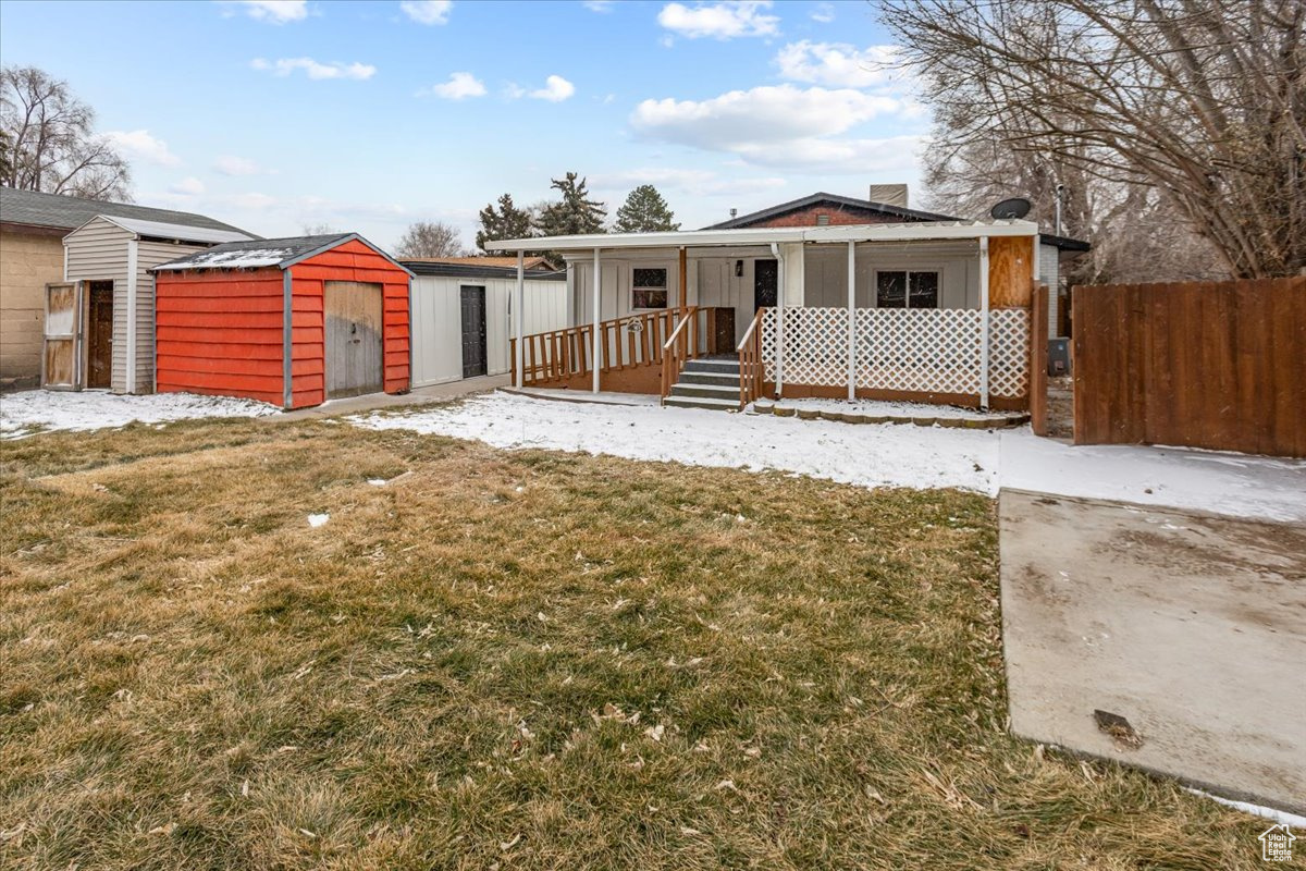 View of back of property featuring a porch, a storage unit, and a backyard