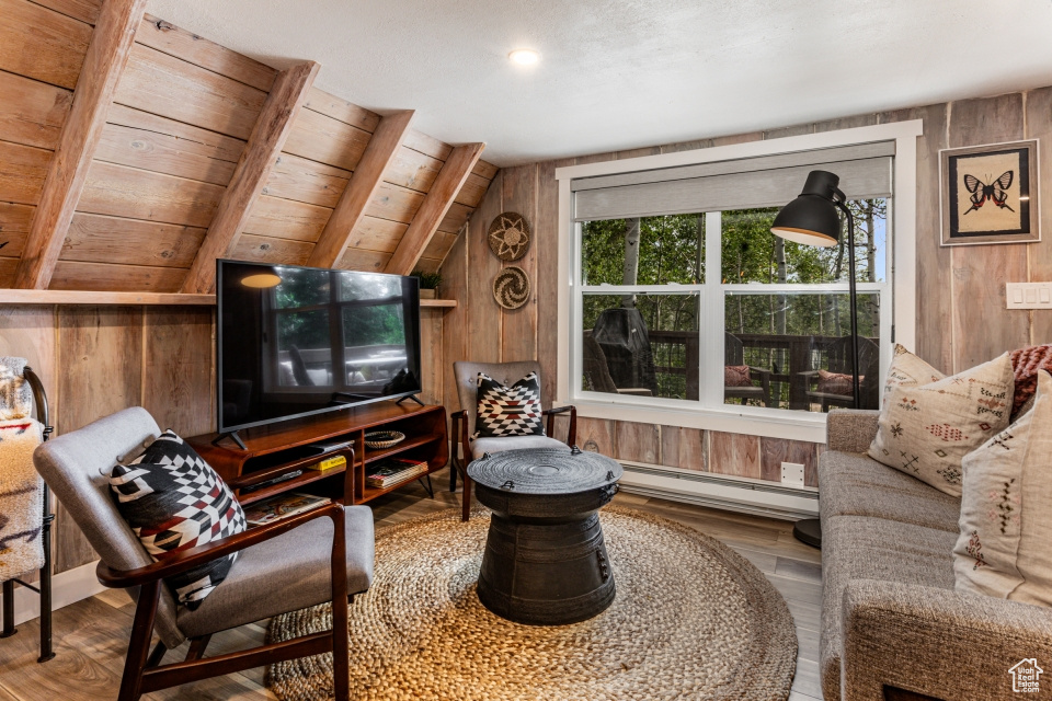 Living area featuring wood walls, vaulted ceiling, hardwood / wood-style floors, and a baseboard heating unit