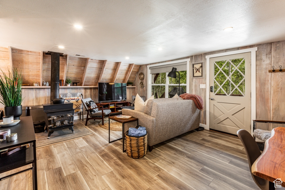 Living room featuring hardwood / wood-style flooring, lofted ceiling, a wood stove, and wood walls