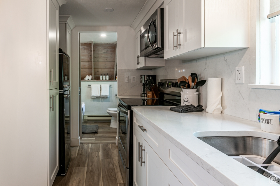 Kitchen featuring tasteful backsplash, appliances with stainless steel finishes, dark hardwood / wood-style floors, and white cabinets