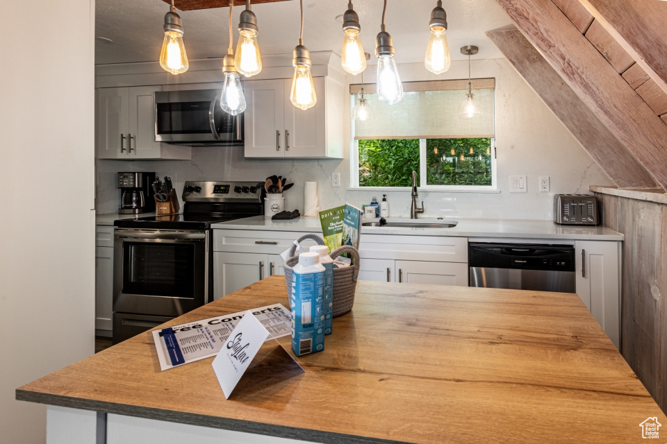 Kitchen featuring white cabinetry, sink, decorative light fixtures, and stainless steel appliances