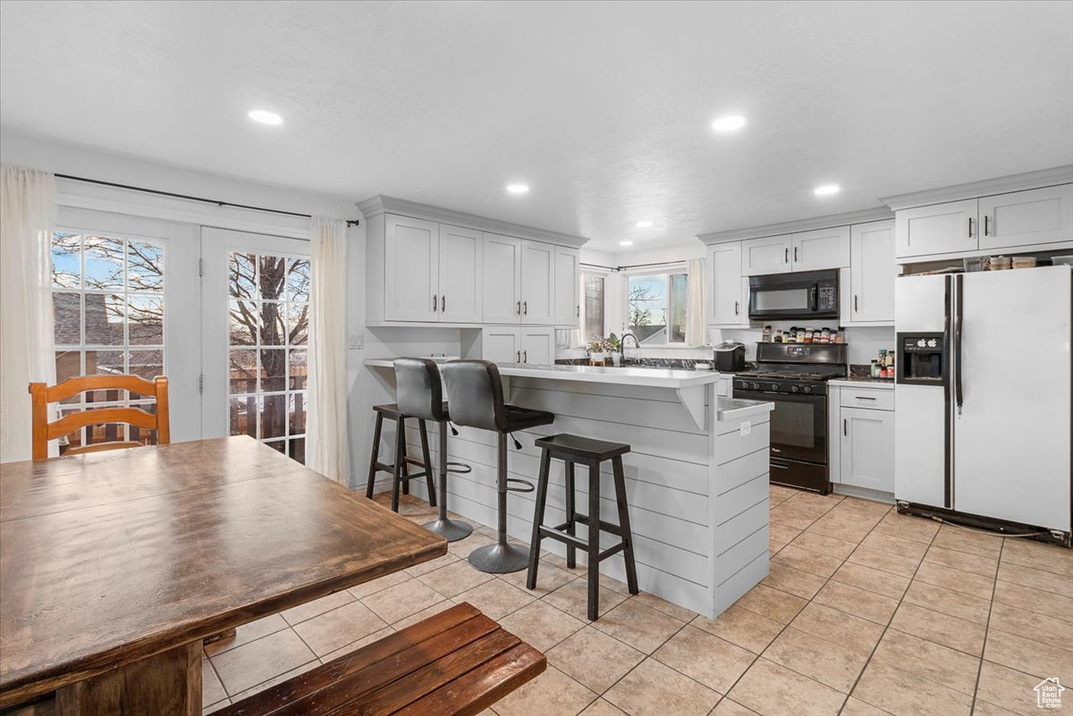 Kitchen featuring white cabinetry, a kitchen breakfast bar, and black appliances