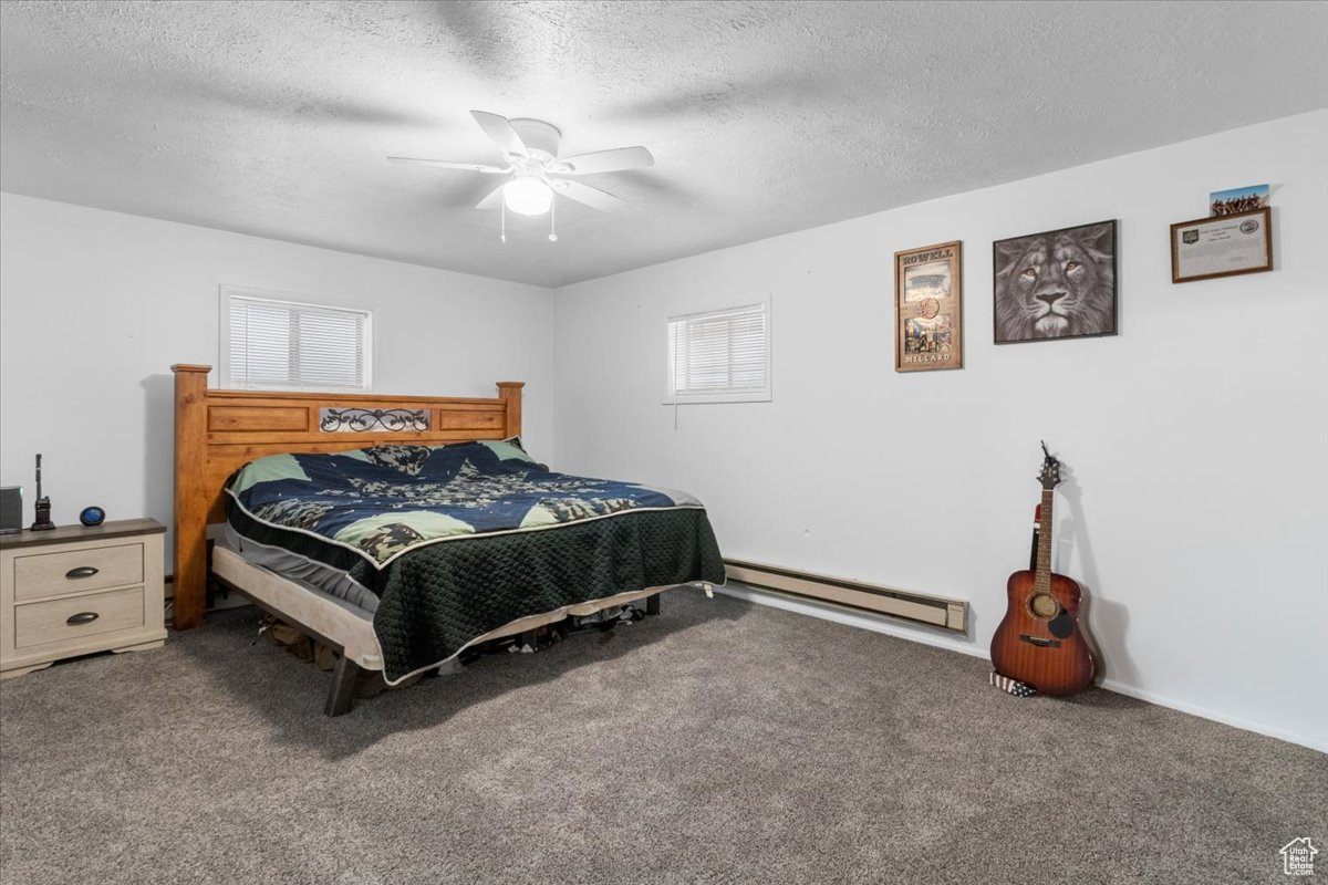Oversized Bedroom with a big walk-in closet, ceiling fan, a baseboard radiator, carpet, and a textured ceiling