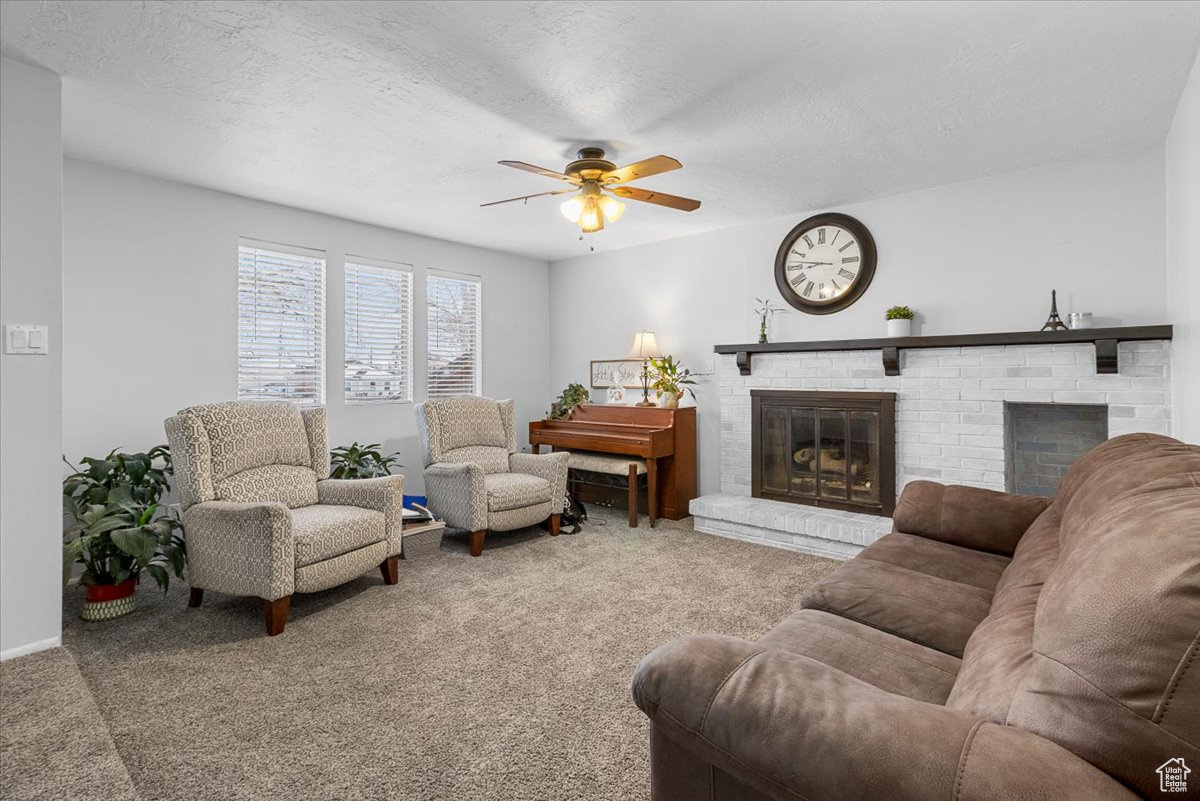 Carpeted living room featuring ceiling fan, a brick fireplace, and a textured ceiling
