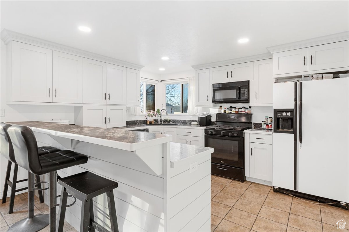 Kitchen with sink, black appliances, light tile patterned floors, a kitchen breakfast bar, and white cabinets