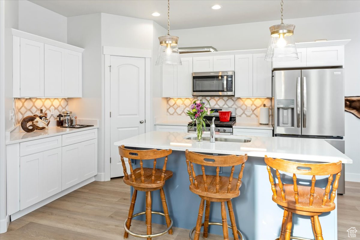 Kitchen featuring pendant lighting, an island with sink, white cabinets, light hardwood / wood-style floors, and stainless steel appliances