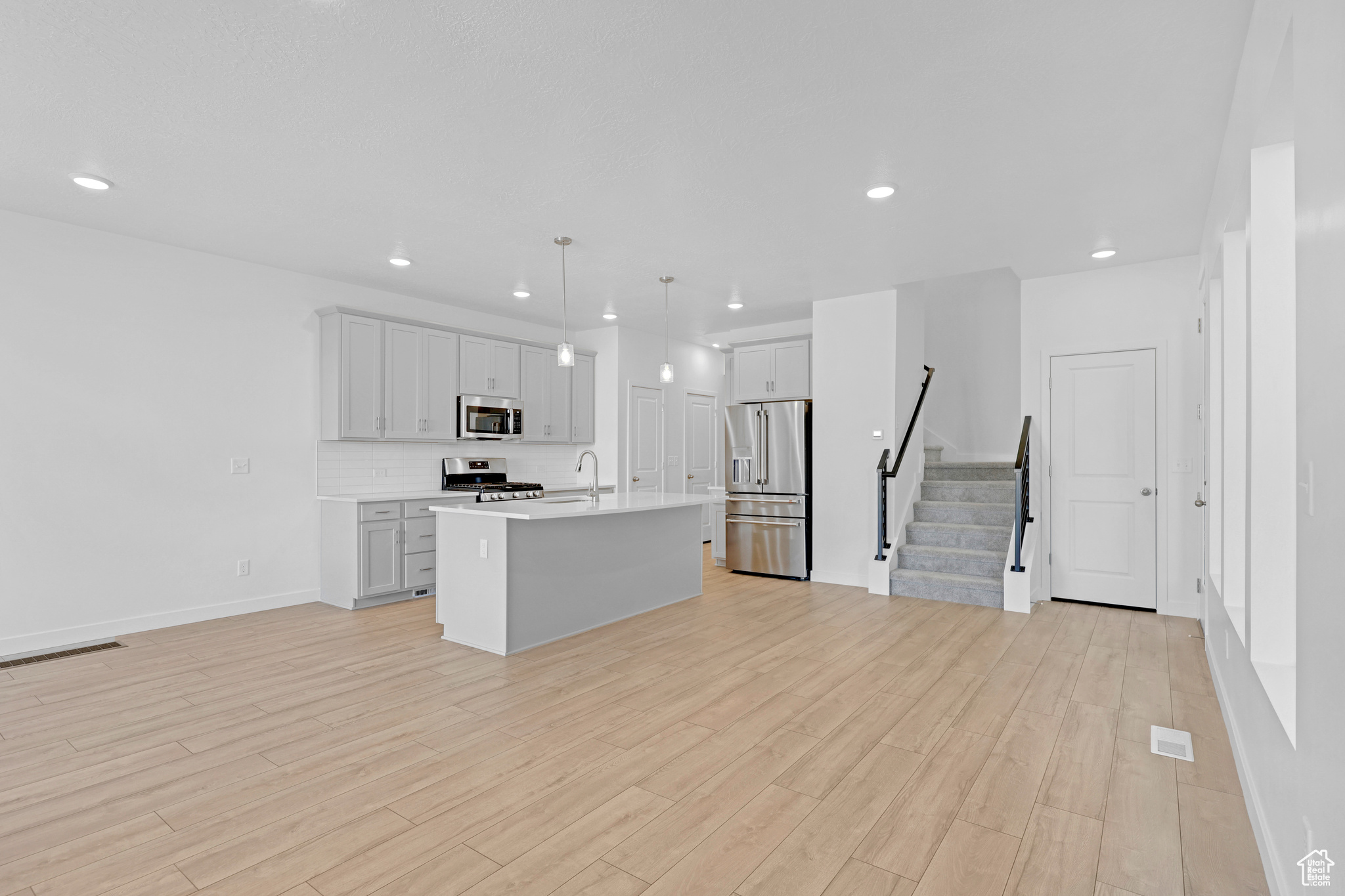 Kitchen with a kitchen island with sink, decorative light fixtures, stainless steel appliances, and light hardwood / wood-style floors