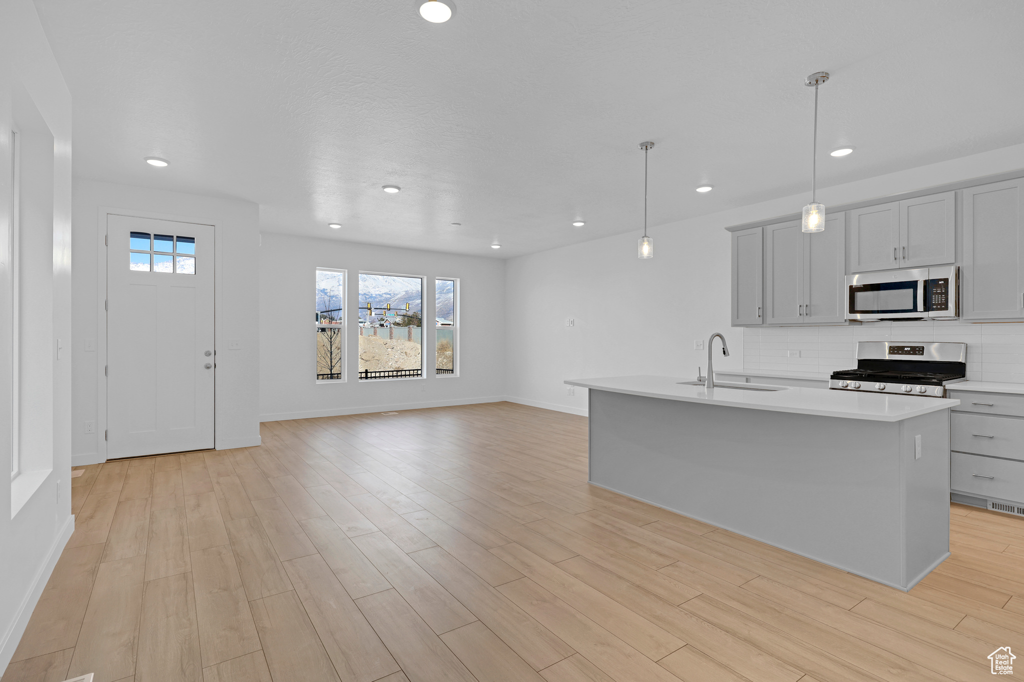 Kitchen with stainless steel appliances, decorative light fixtures, sink, and a center island with sink