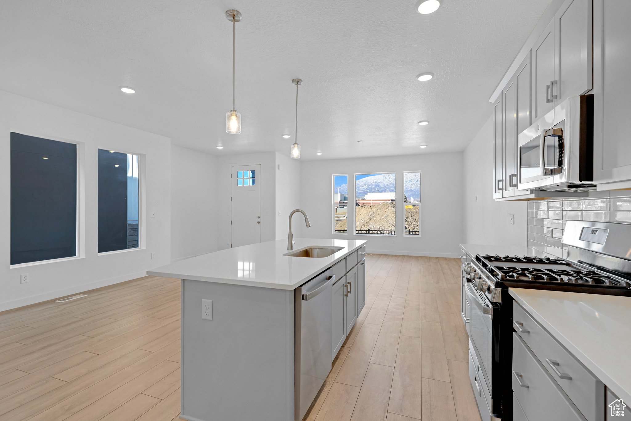 Kitchen featuring sink, appliances with stainless steel finishes, an island with sink, decorative light fixtures, and light wood-type flooring