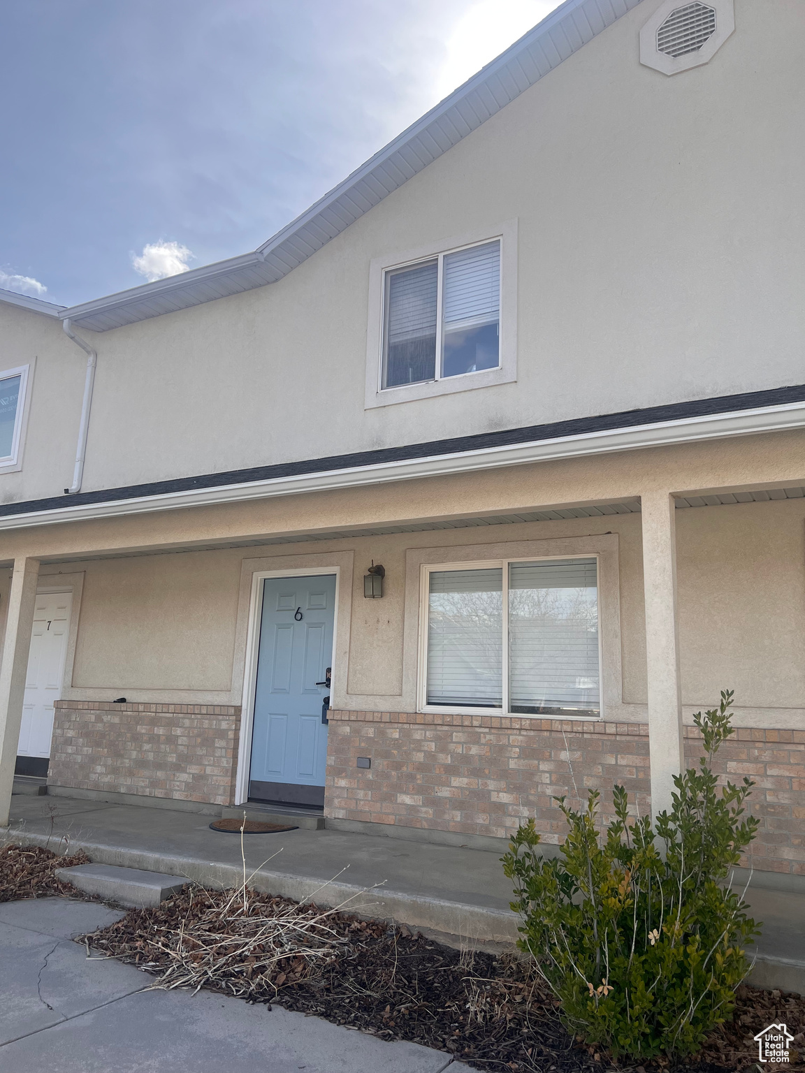 Exterior space with stucco siding, visible vents, covered porch, and brick siding