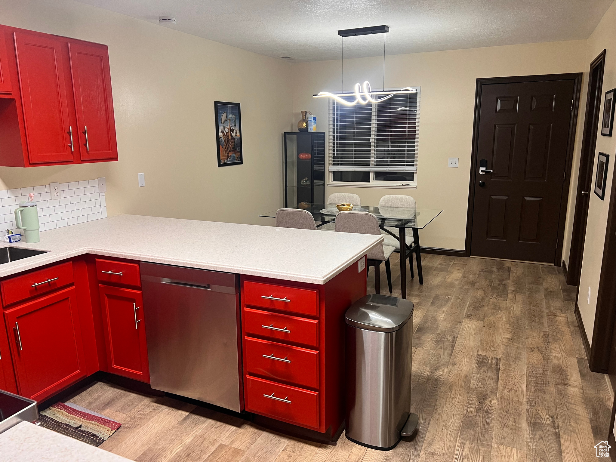 Kitchen with decorative light fixtures, wood-type flooring, kitchen peninsula, and dishwasher
