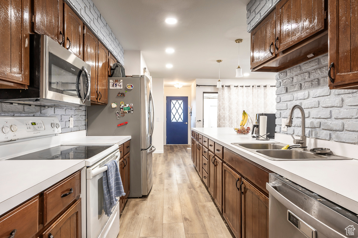 Kitchen featuring pendant lighting, sink, backsplash, stainless steel appliances, and light hardwood / wood-style floors