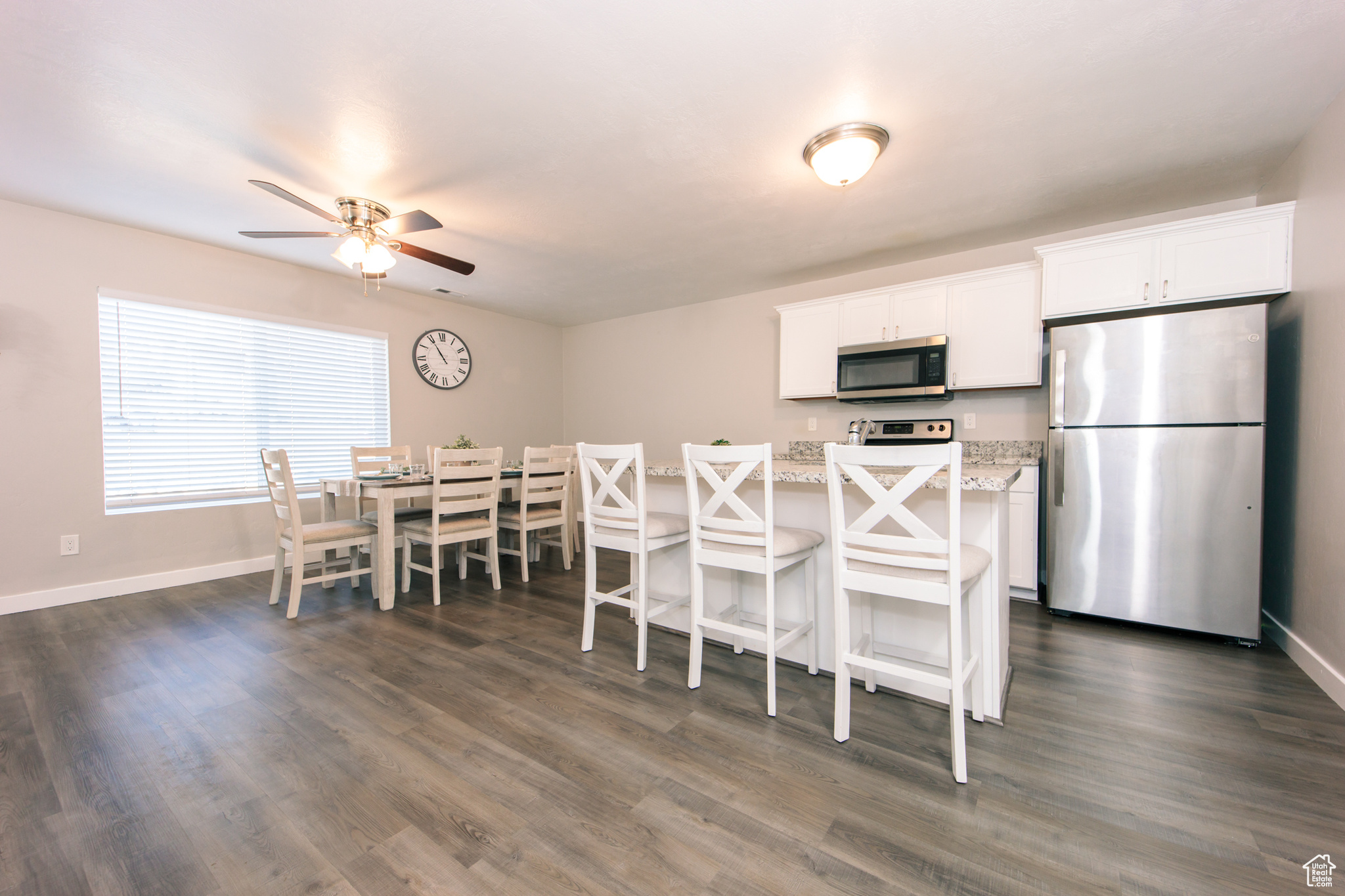 Kitchen with dark hardwood / wood-style floors, white cabinets, a kitchen bar, light stone counters, and stainless steel appliances