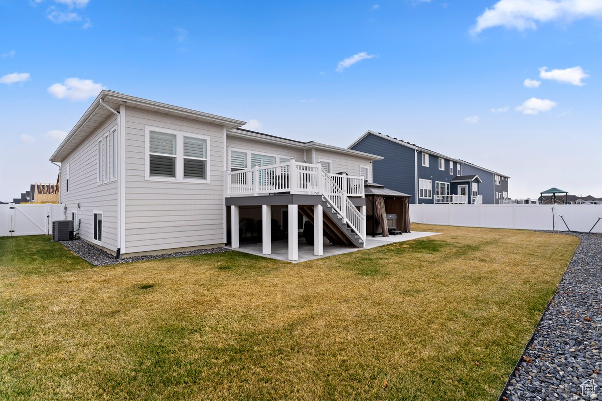 Back of property with central AC unit, a lawn, a patio, and a deck