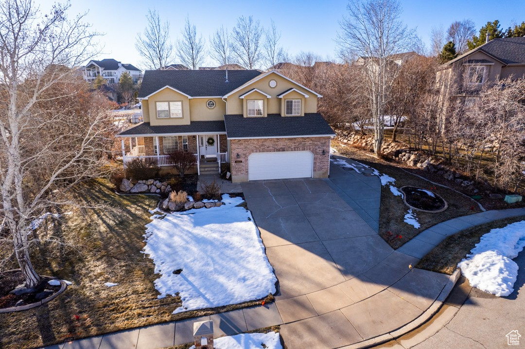 Traditional-style home featuring an attached garage, covered porch, driveway, stone siding, and stucco siding