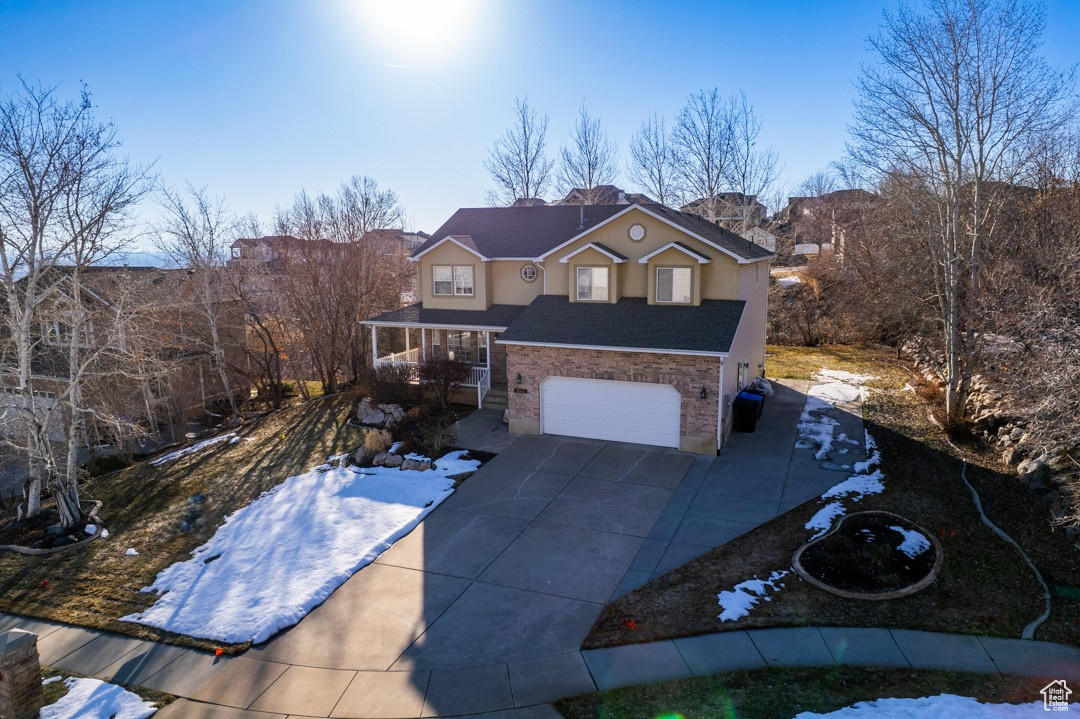 Traditional-style home with an attached garage, covered porch, stone siding, concrete driveway, and stucco siding