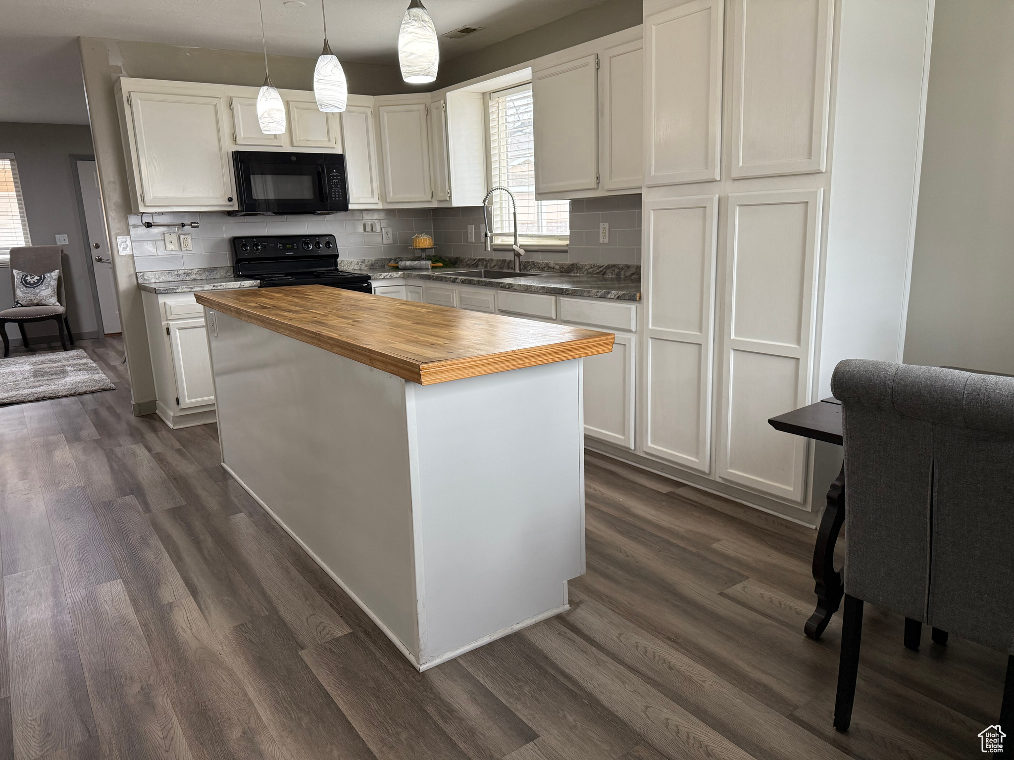 Kitchen with dark wood-style floors, wooden counters, a sink, black appliances, and white cabinetry