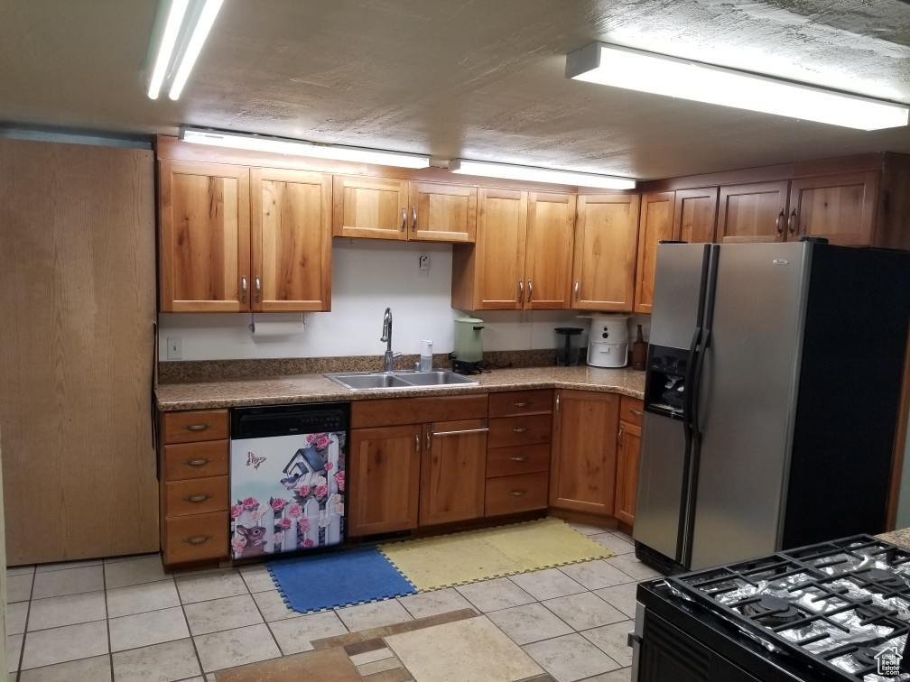Kitchen with dishwashing machine, brown cabinetry, a sink, black gas range, and stainless steel refrigerator with ice dispenser