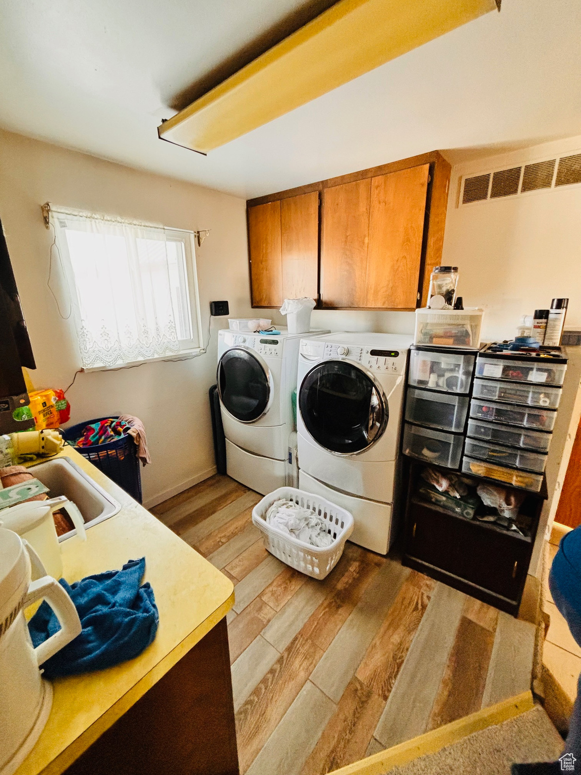 Laundry room with visible vents, a sink, cabinet space, light wood-style floors, and washing machine and clothes dryer