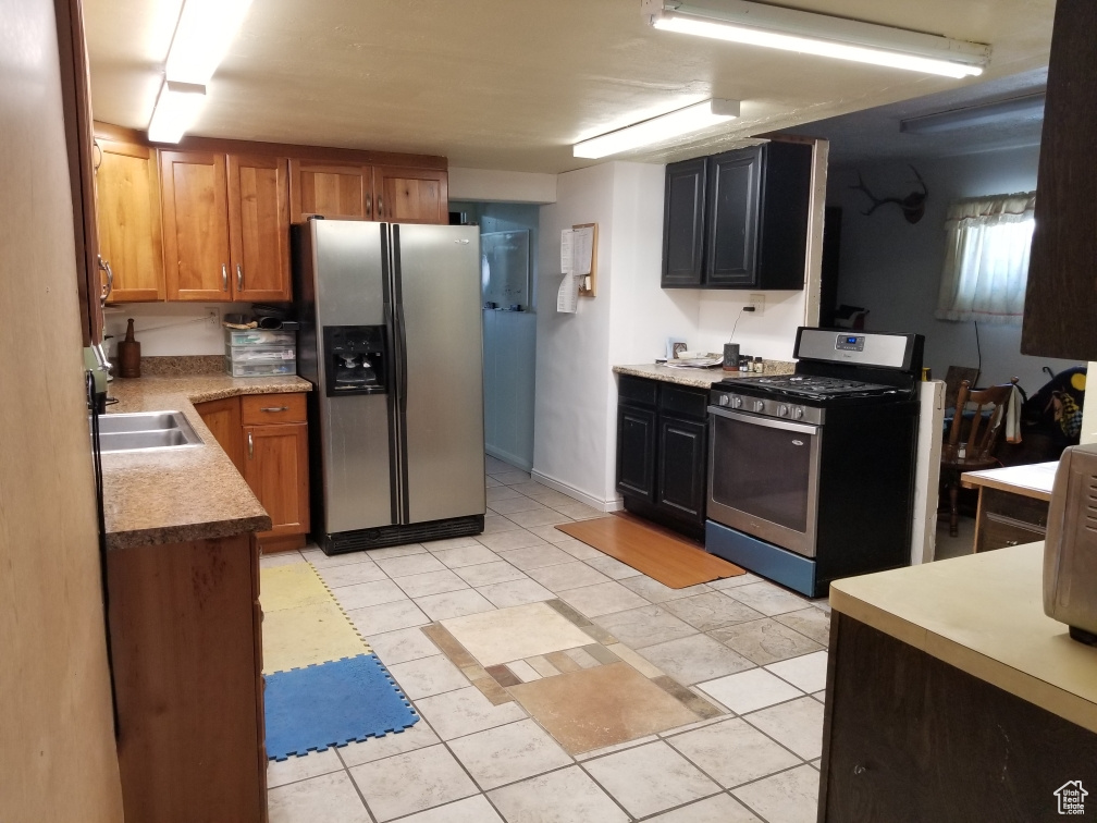 Kitchen with light countertops, brown cabinets, light tile patterned flooring, stainless steel appliances, and a sink