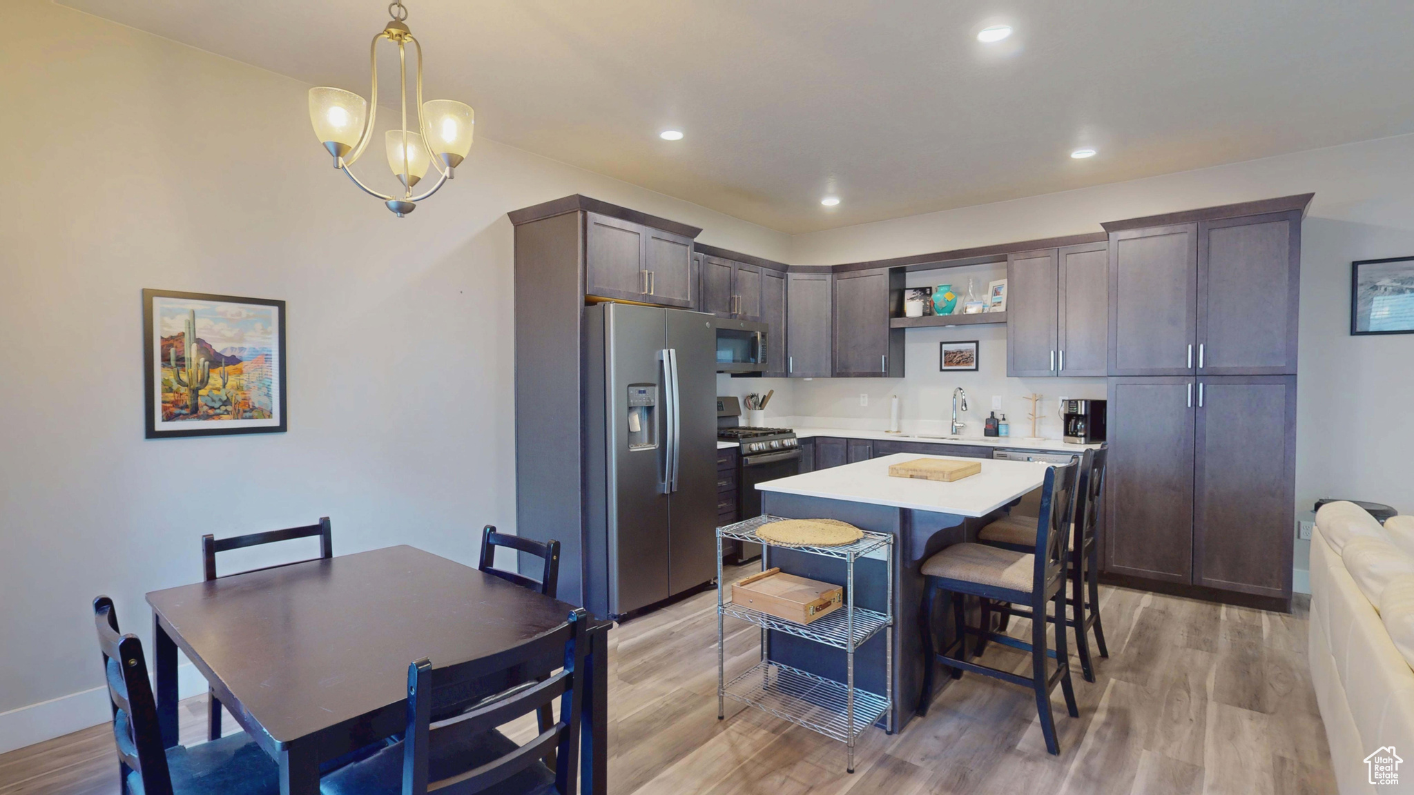 Kitchen featuring a kitchen island, appliances with stainless steel finishes, decorative light fixtures, dark brown cabinetry, and light hardwood / wood-style flooring