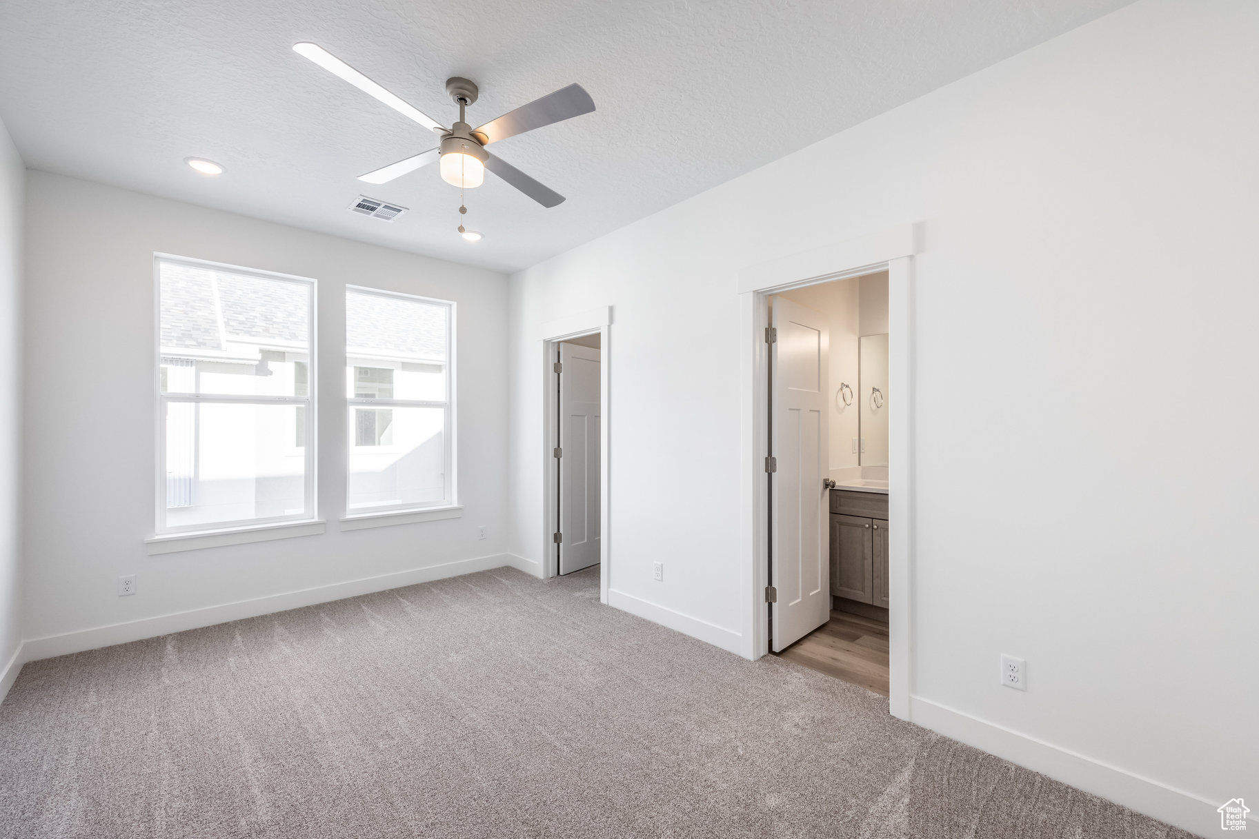 Unfurnished bedroom with ceiling fan, ensuite bath, light carpet, and a textured ceiling