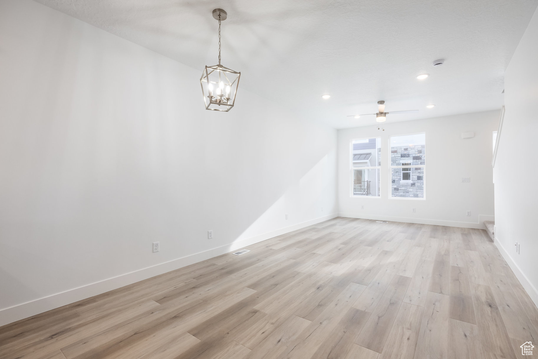 Spare room with ceiling fan with notable chandelier and light hardwood / wood-style flooring