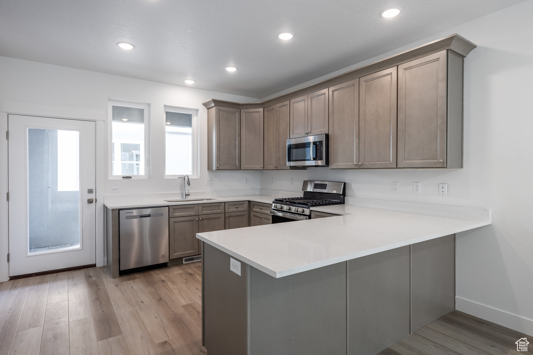 Kitchen with sink, light hardwood / wood-style flooring, kitchen peninsula, and appliances with stainless steel finishes