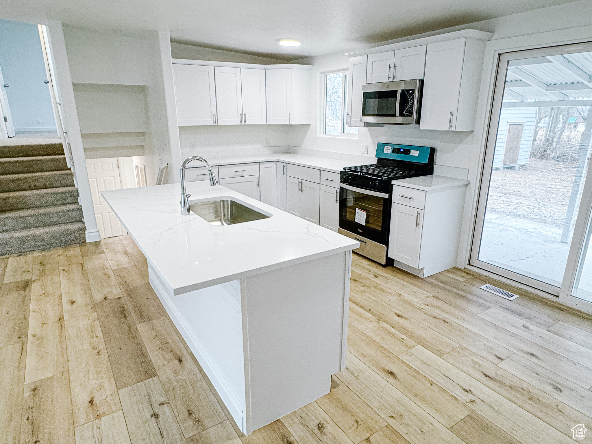 Kitchen featuring stainless steel appliances, a kitchen island with sink, sink, and white cabinets